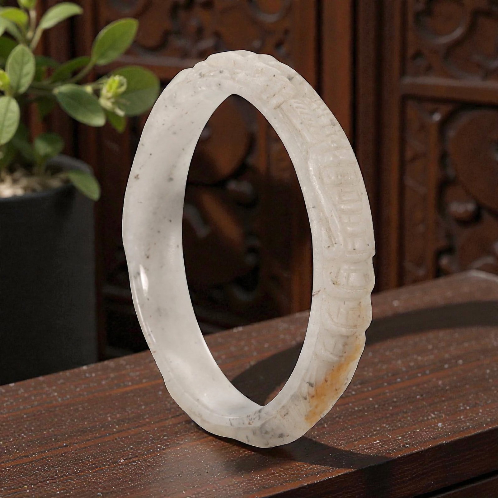 A Chinese Carved Jadeite Jade Bangle Bracelet, 20th Century, 54ZL: A fine jadeite bangle of flattened circular form, masterfully carved in relief with a continuous band of archaistic scroll motifs. The stone exhibits a translucent pale white base, accented by subtle 