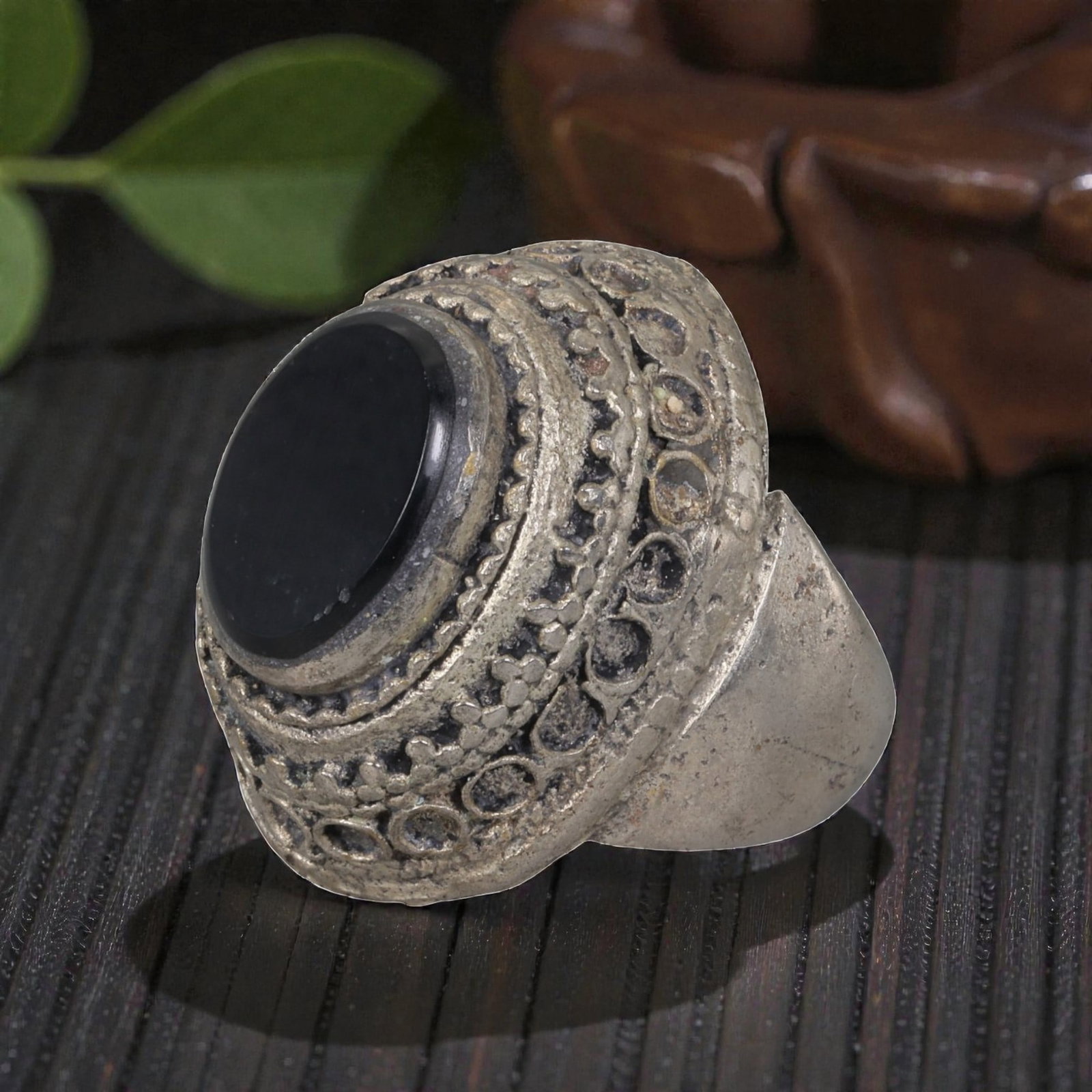 A Middle Eastern Silver Plated Onyx Ring, Late 19th-Early 20th Century, 20AK: The ring is centered with a round cabochon onyx stone, set within a multi-layered bezel featuring raised floral motifs and rows of empty circular settings. The surface displays patina, surface wear, a