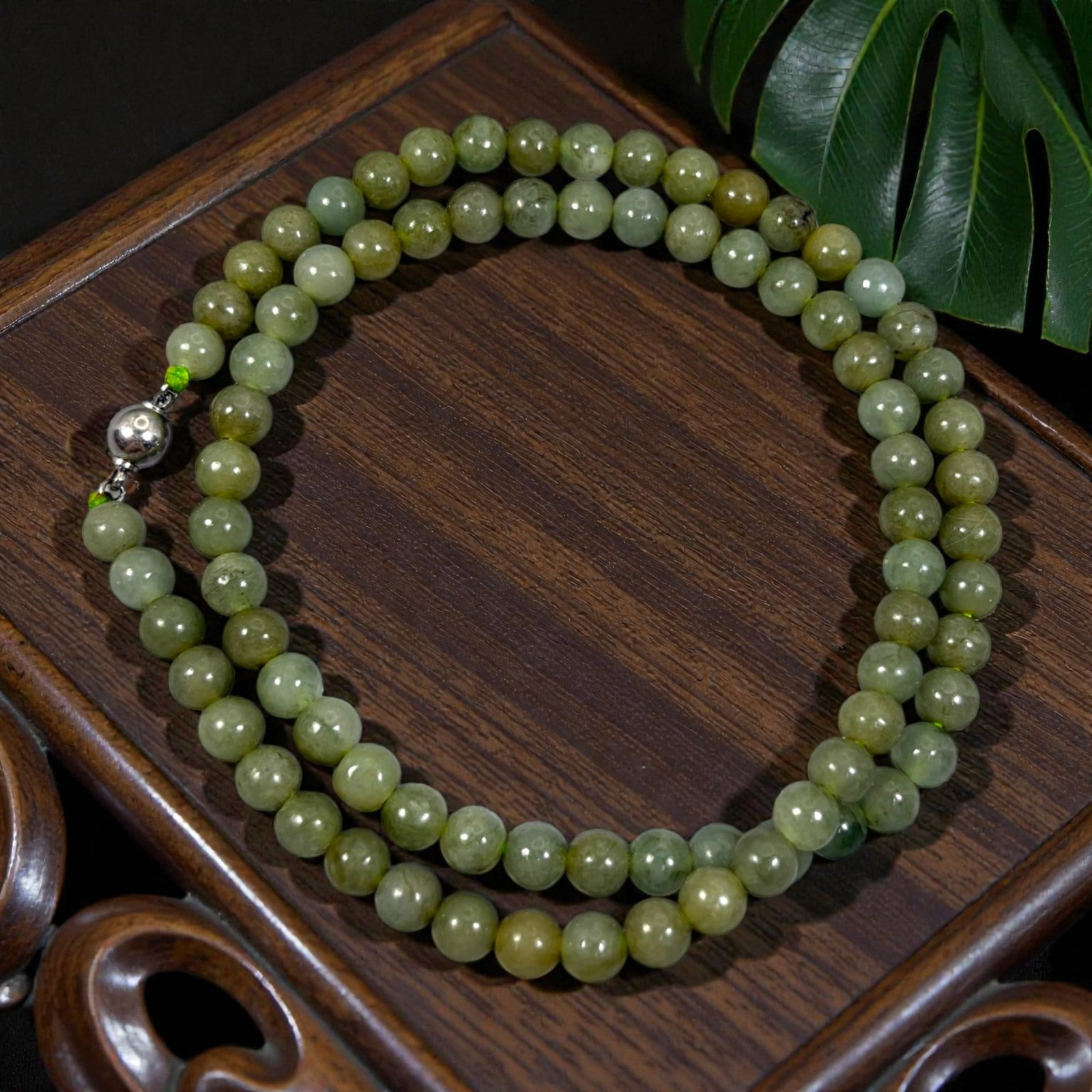 Chinese Jadeite Jade Bead Necklace, 20th Century, 90XC: A continuous strand of polished jadeite beads, each of uniform spherical form, displaying soft olive-green and light yellow-green tones with natural mineral inclusions and subtle variations in translu