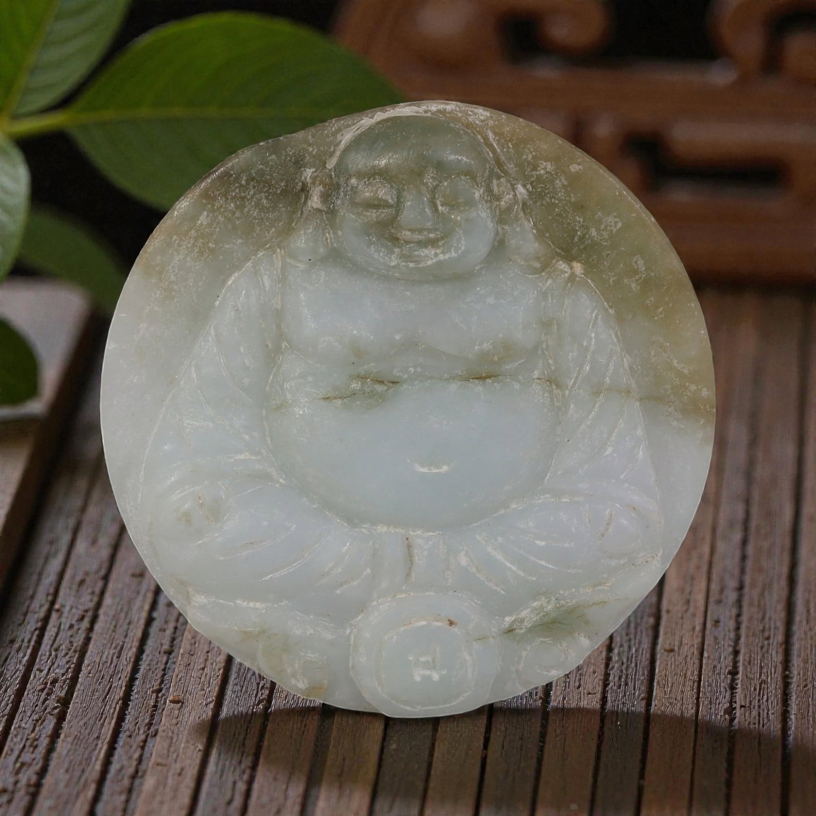 Old Chinese Jadeite Jade Budai Pendant, 13AP: Carved from jadeite jade with pale green and light brownish inclusions, the pendant depicts Budai (the Laughing Buddha) in a seated pose. The figure features a rounded face with closed eyes and a smil