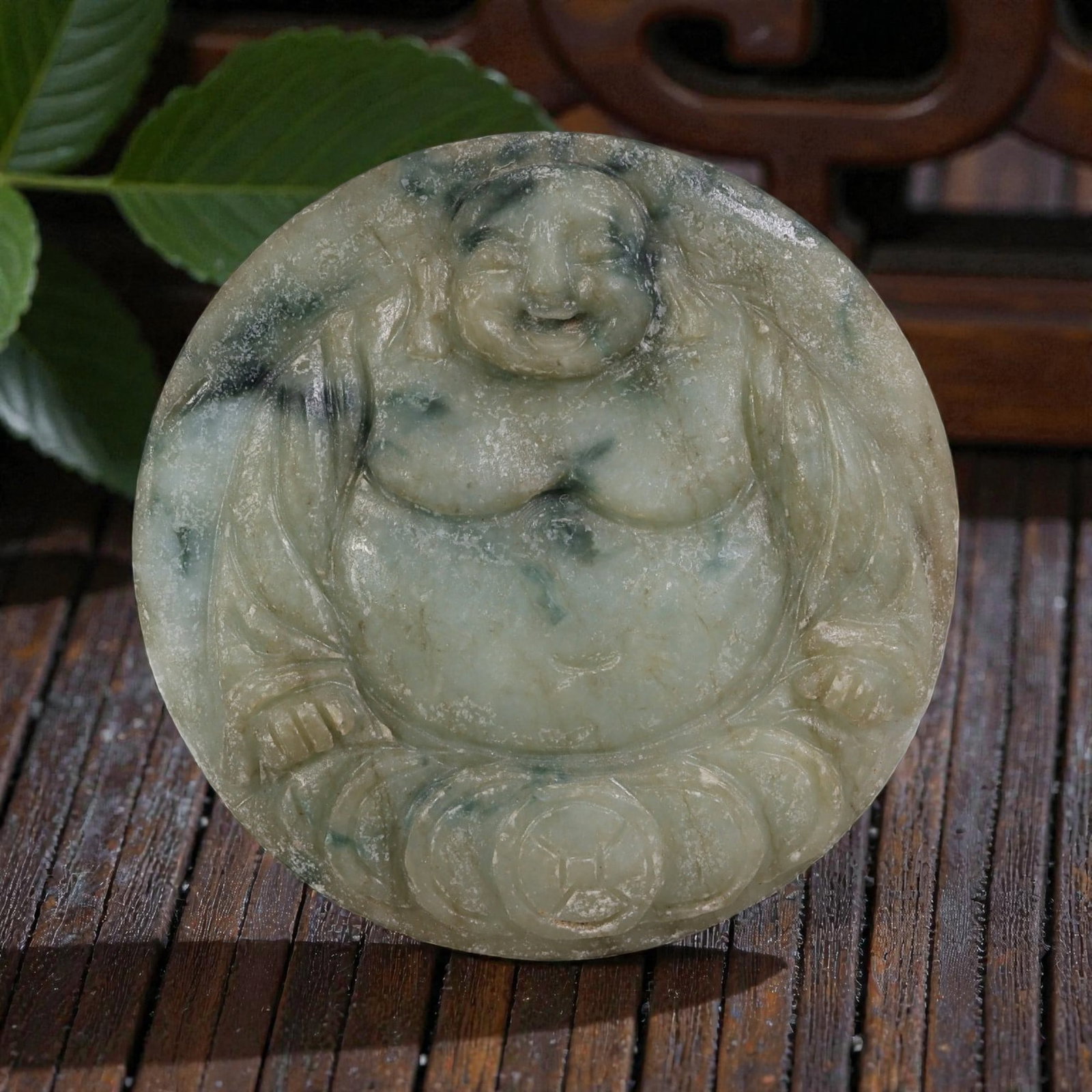 Old Chinese Jadeite Jade Budai Pendant, 10AP: Carved from jadeite jade with light green and mottled dark green inclusions, the pendant depicts Budai (the Laughing Buddha) in a seated pose. The figure has a rounded face with closed eyes and a smil