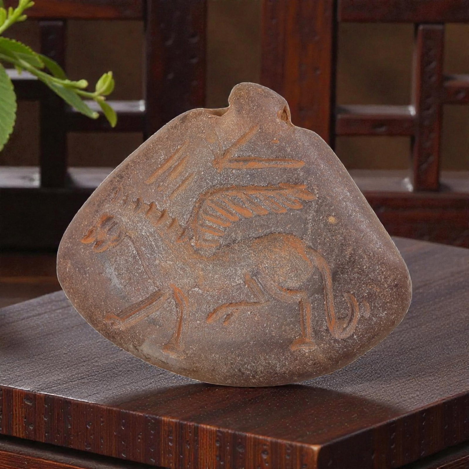 Ancient Sasanian Chalcedony Amulet Pendant, 55YD: This ancient amulet pendant is carved from weathered, translucent dark chalcedony, with a fan-shaped form and suspension lug at the top. The face features a deeply engraved intaglio depicting a winged