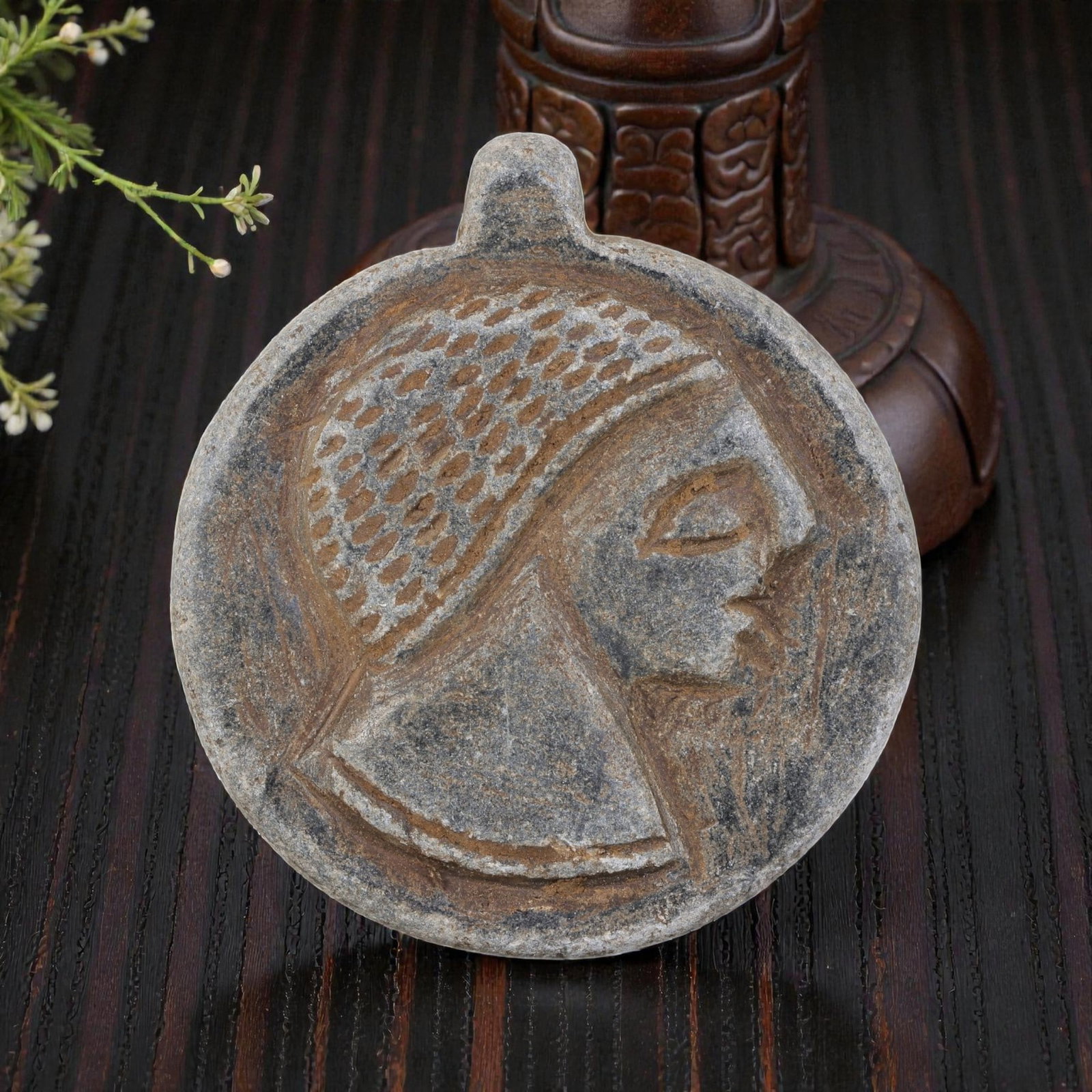Antique Medieval Islamic Carved Stone Amulet with Profile Head Motif, 43YD: This antique amulet is carved from weathered grey stone, featuring a circular form with a suspension loop at the top. The face displays a deeply incised profile of a human head, adorned with a pattern