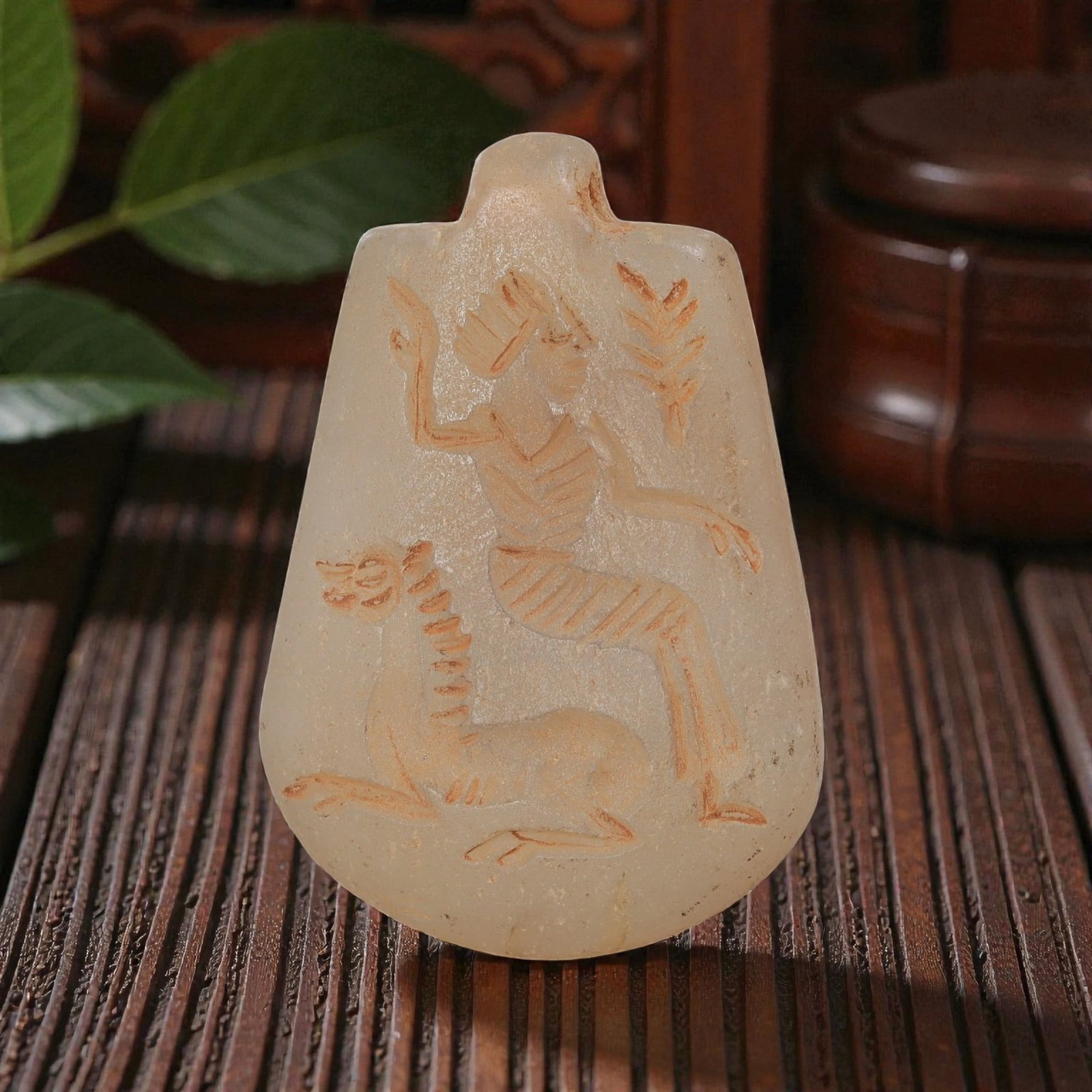 Ancient Sasanian Chalcedony Amulet Pendant, 56YD: This ancient amulet pendant is carved from translucent pale chalcedony, with a tapered shield-shaped form and suspension lug at the top. The face features a deeply engraved intaglio depicting a seated