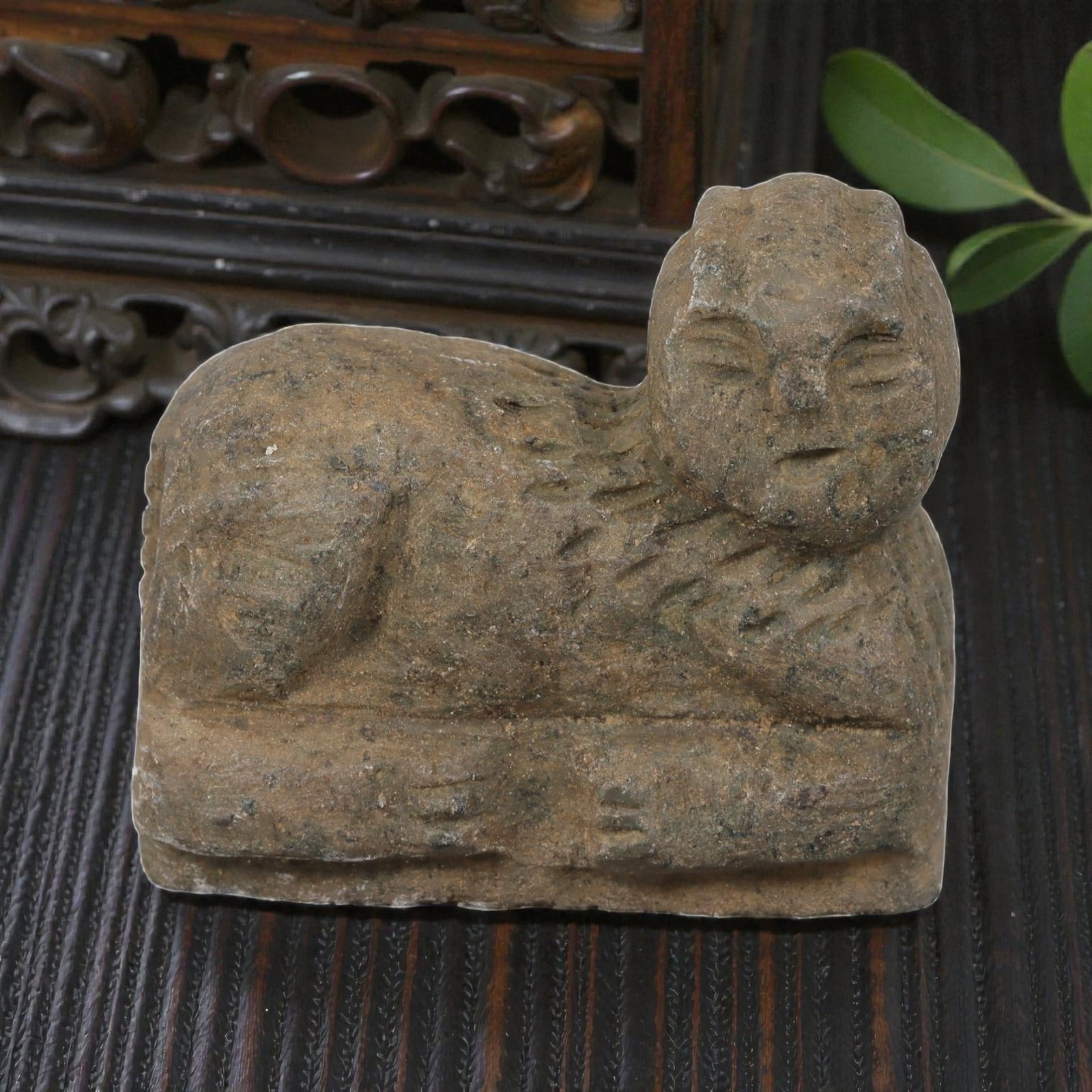 Ancient Near Eastern Recumbent Stone Feline Amulet, 41YD: This ancient amulet is carved from weathered grey-brown stone, depicting a recumbent stylized feline resting on a rectangular base. The creature features a humanized face with incised eyes and mouth, 