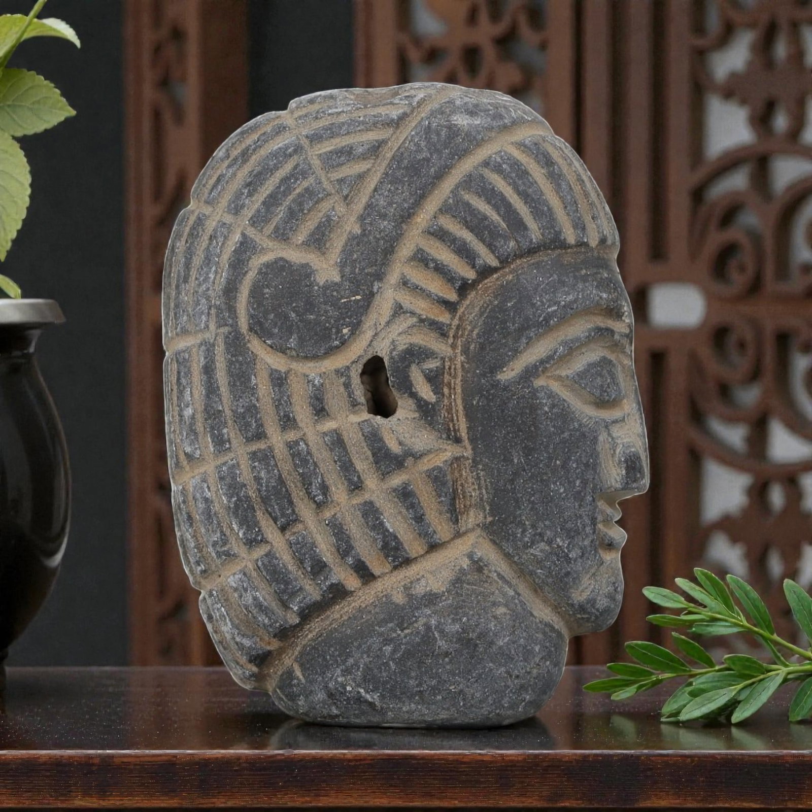 Antique Egyptian Schist Intaglio with Profile Head Motif, 43AP: Carved from dark grey schist, this oval profile head features deeply incised linear patterns representing the headdress and hairstyle, with earthy deposits filling the carved recesses. The simplified 
