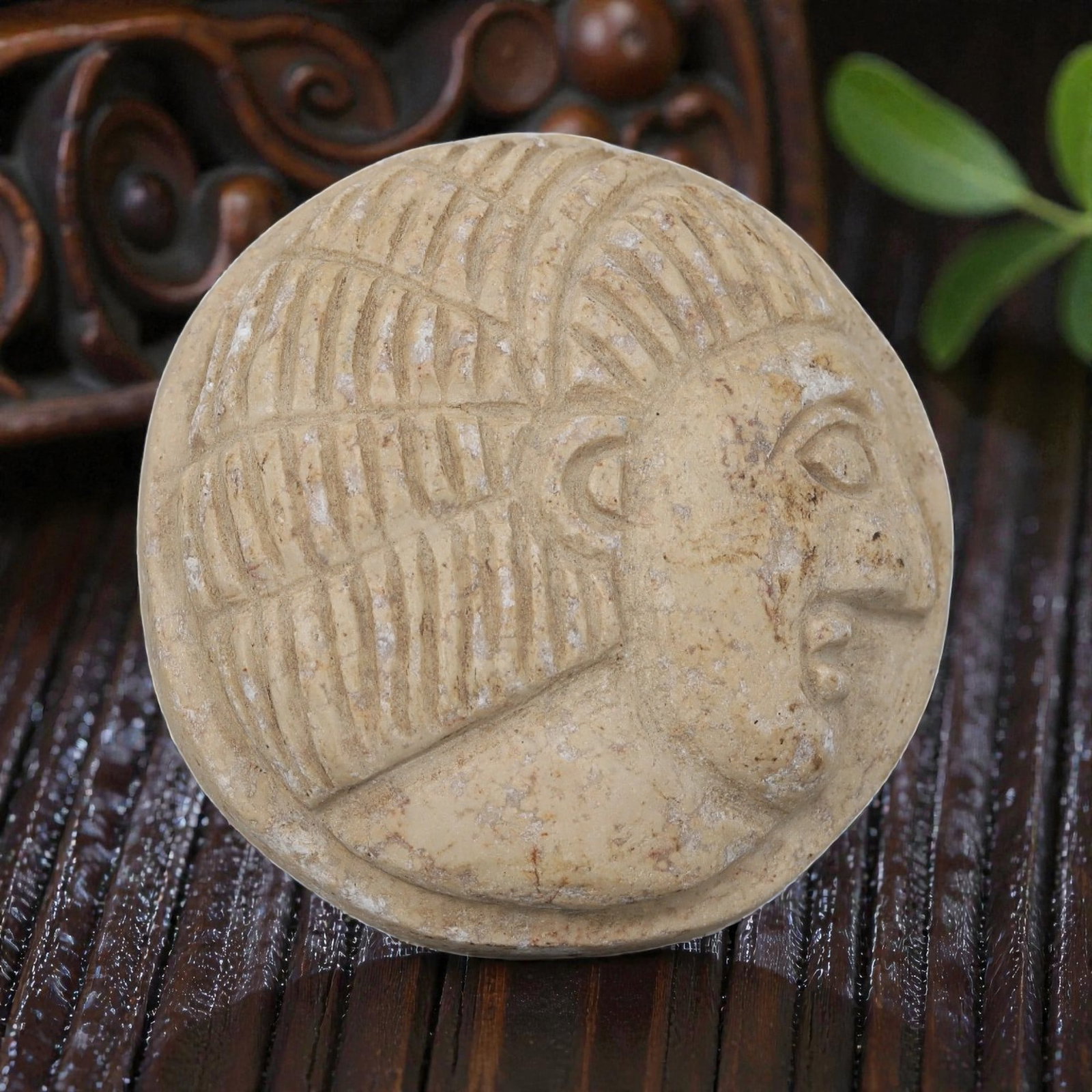 Antique Egyptian Steatite Intaglio with Profile Head Motif, 40AP: Carved from light beige steatite, this circular intaglio features a raised relief profile head with deeply incised linear patterns representing the hairstyle and headdress, alongside simplified facial