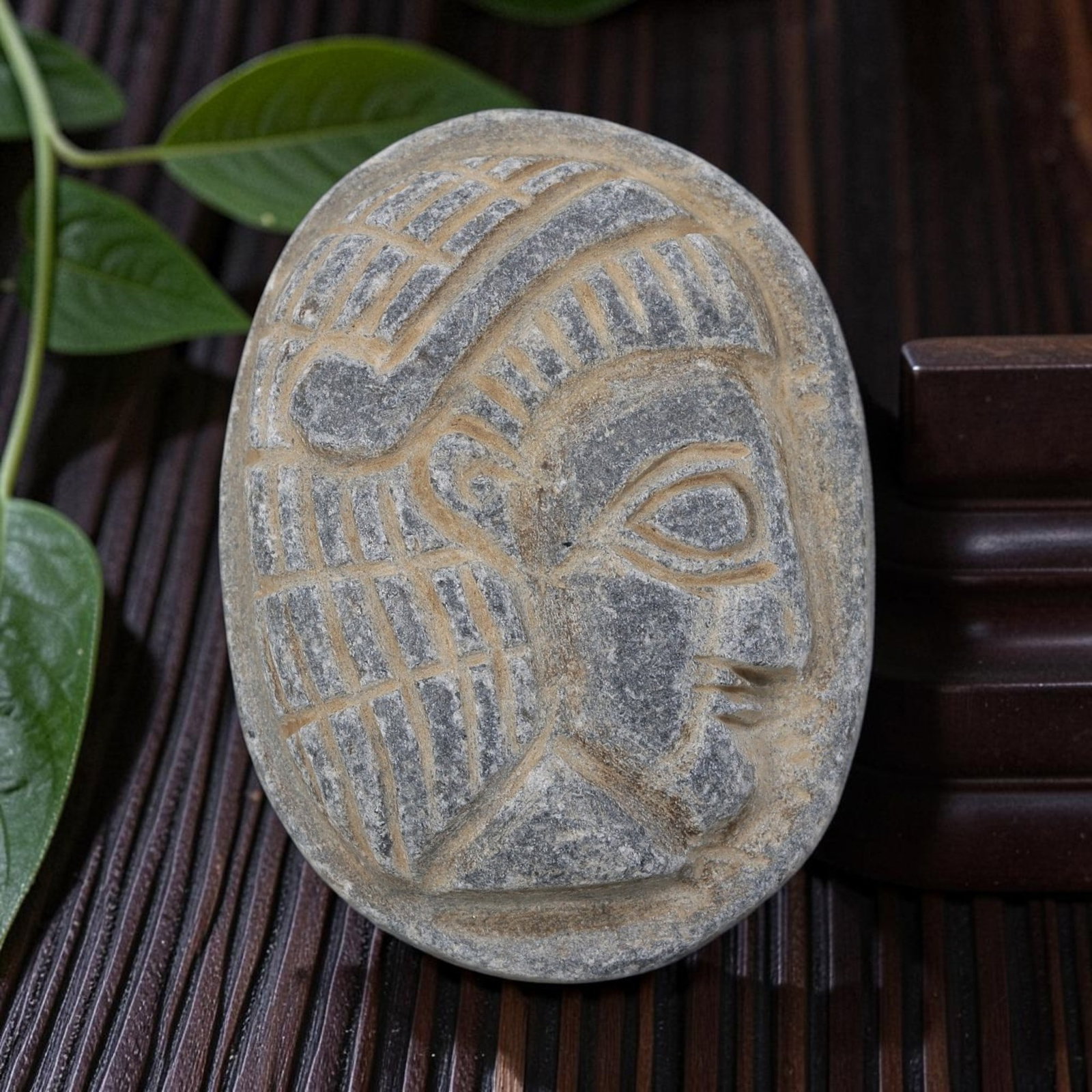 Antique Egyptian Schist Intaglio with Profile Head Motif, 36AP: Carved from dark grey schist, this oval intaglio depicts a stylized human head in profile with deeply incised grid and linear patterns representing the headdress and hairstyle, alongside simplified fa