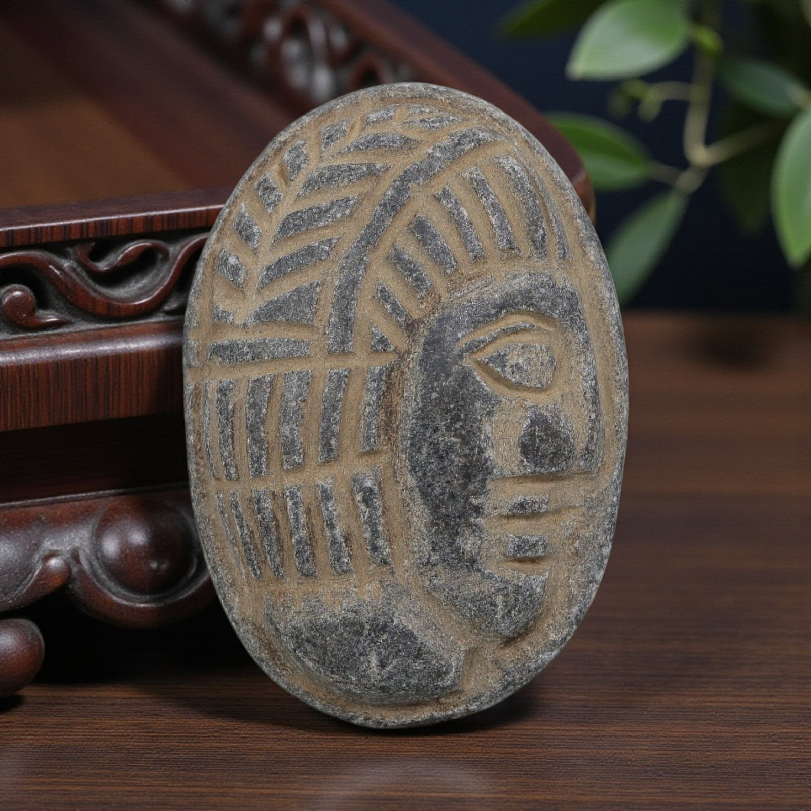 Antique Egyptian Schist Intaglio with Profile Head Motif, 99YD: Carved from dark grey schist, this oval intaglio depicts a stylized human head in profile, with deeply incised linear patterns representing the headdress and hairstyle, alongside simplified facial fea