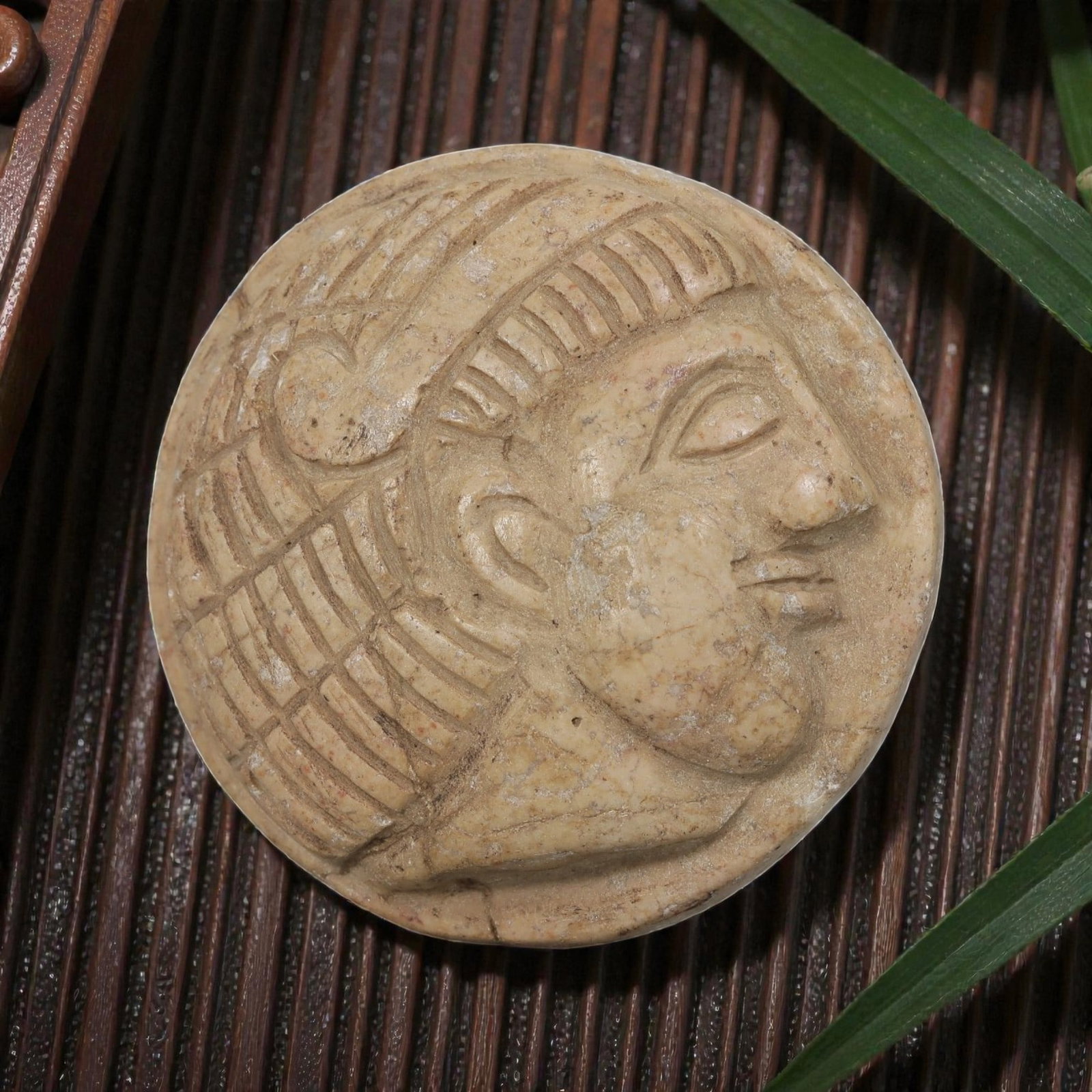Antique Egyptian Steatite Intaglio with Profile Head Motif, 41AP: Carved from pale beige steatite, this circular intaglio features a raised relief profile head with incised grid and linear patterns representing the headdress and hairstyle, alongside defined facial f