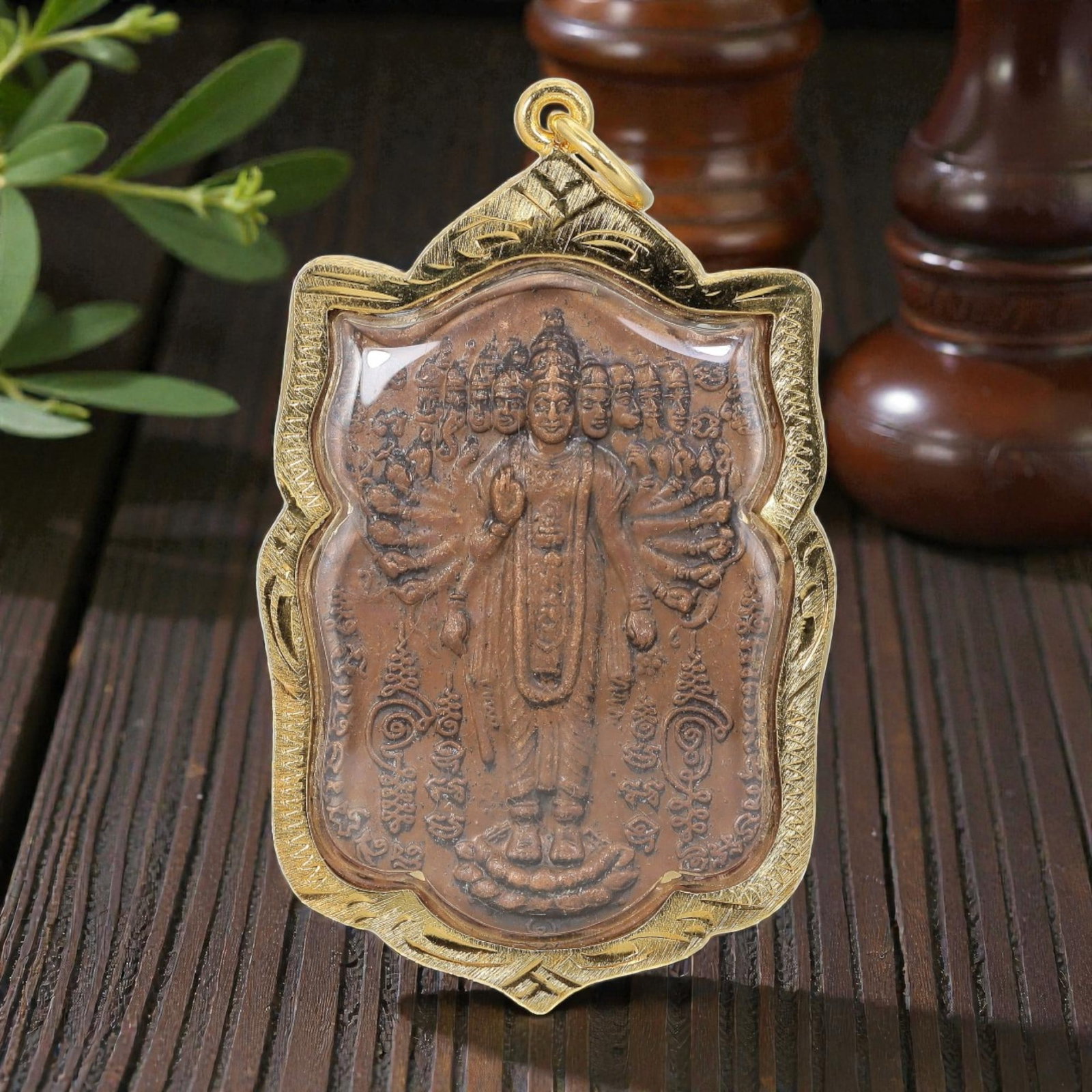 Thai Multi-Armed Deity Amulet - Gold Tone Pendant, 48AP: A Thai Buddhist amulet featuring a multi-headed, multi-armed deity figure, housed in a decorative gold-tone metal casing with a glass-fronted enclosure. The copper-toned plaque displays detailed relie