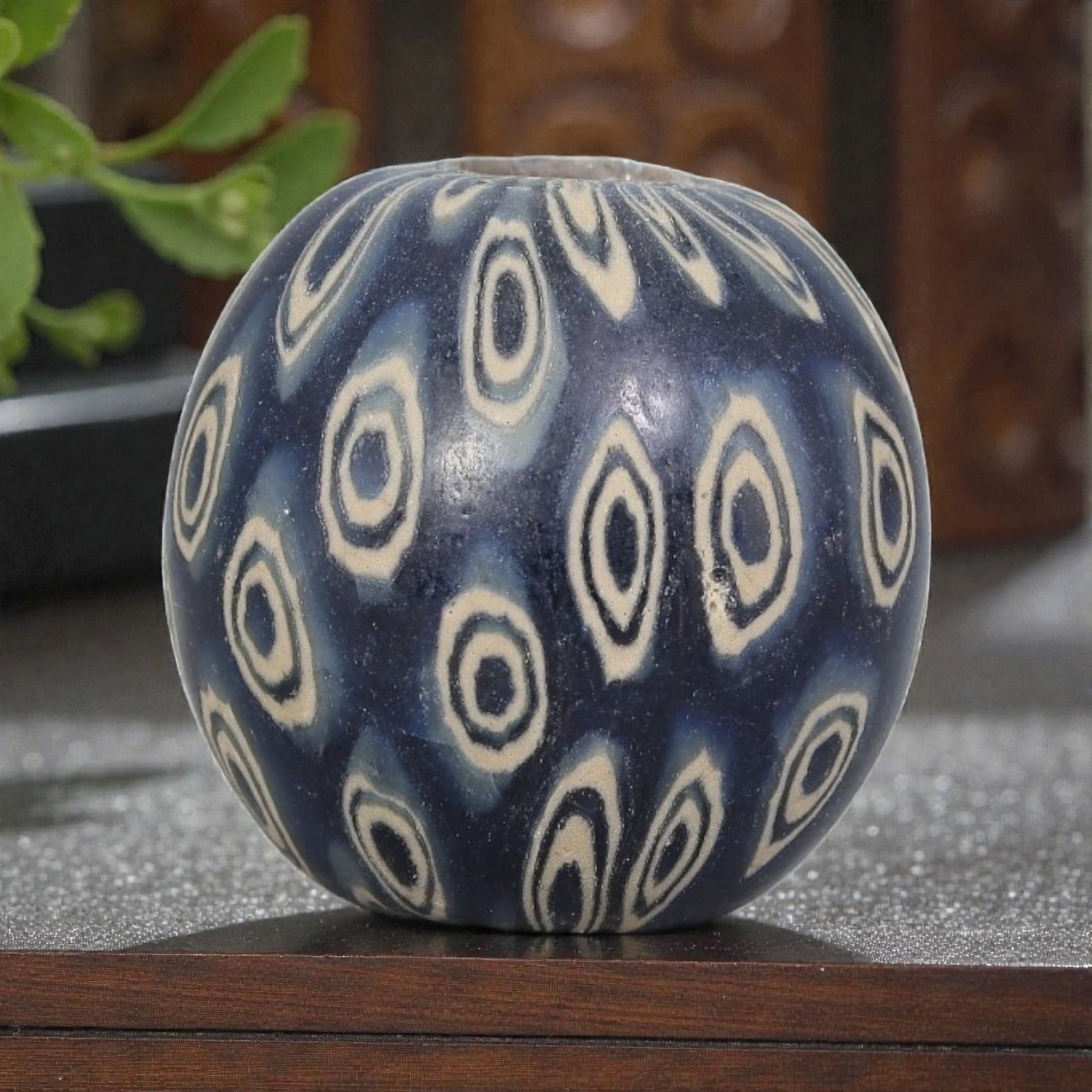 Antique Glass Bead - Islamic Jatim Indigo Concentric Eye Mosaic, 48YH: A spherical glass bead of Islamic Jatim type, crafted from polychrome mosaic glass. The surface features repeating concentric eye motifs with dark centers, framed by light beige rings, set against a r