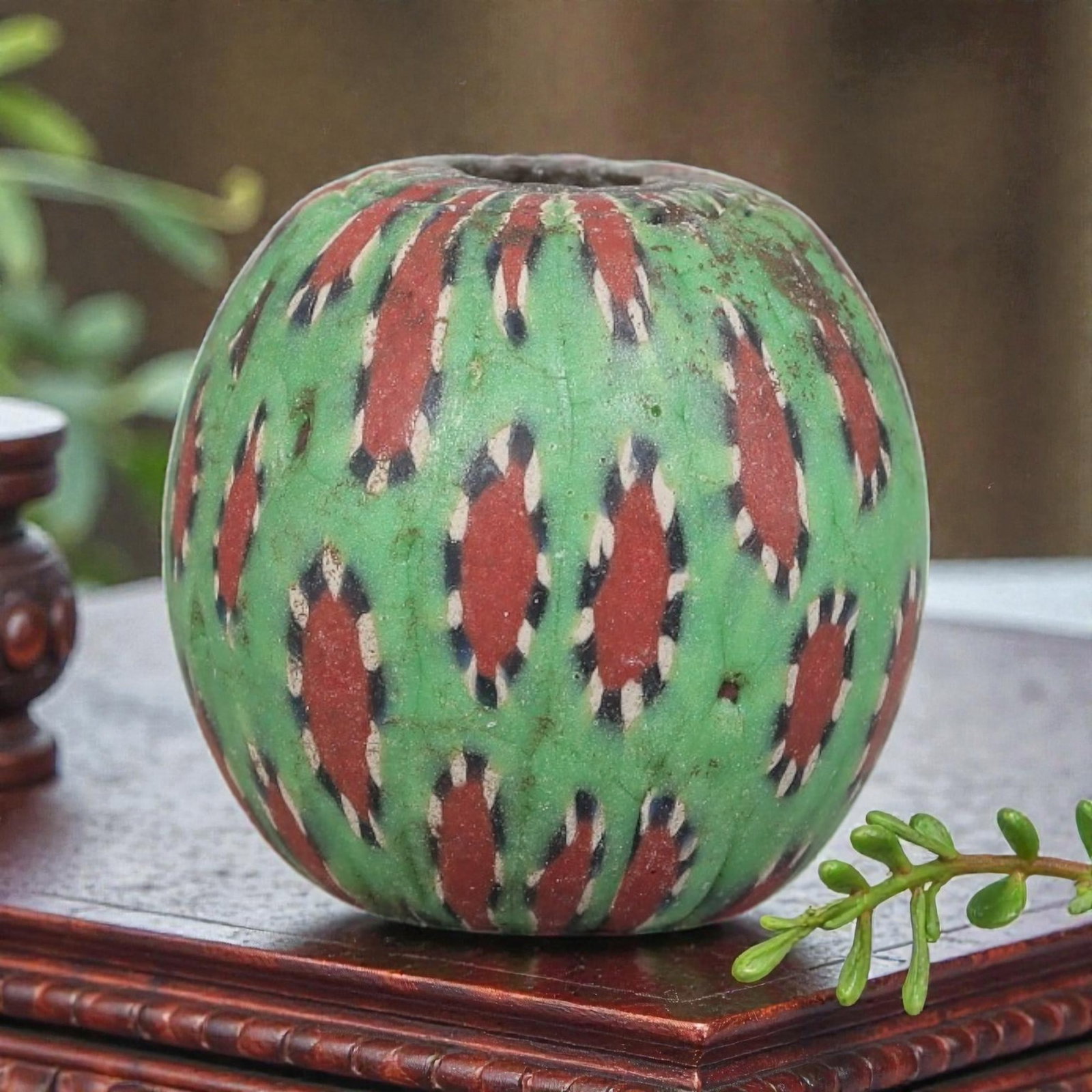Antique Glass Bead - Islamic Jatim Green Ikat Mosaic, 44YH: A spherical glass bead of Islamic Jatim type, crafted from polychrome mosaic glass. The surface features repeating elongated red motifs framed by black and white borders, set against a vibrant green g