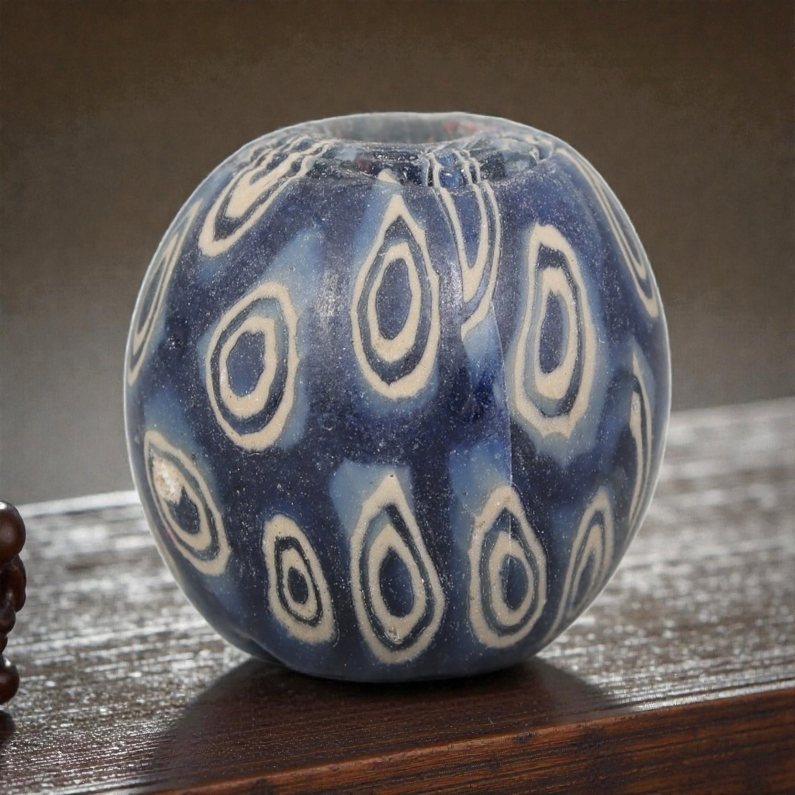Antique Glass Bead - Islamic Jatim Indigo Peacock Eye Mosaic, 73AP: A spherical glass bead of Islamic Jatim type, crafted from polychrome mosaic glass. The surface features repeating teardrop-shaped peacock eye motifs, with layered cream and indigo rings set against a