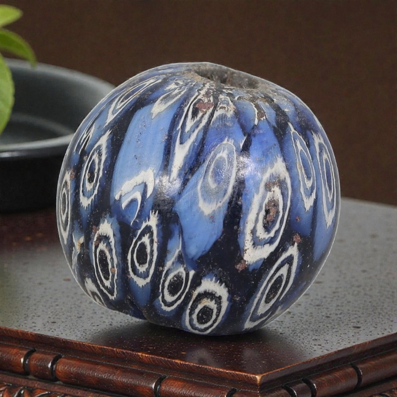 Antique Glass Bead - Islamic Jatim Indigo Swirl Eye Mosaic, 56YH: A spherical glass bead of Islamic Jatim type, crafted from polychrome mosaic glass. The surface features repeating concentric eye motifs with dark centers and white fringed borders, set against a swir
