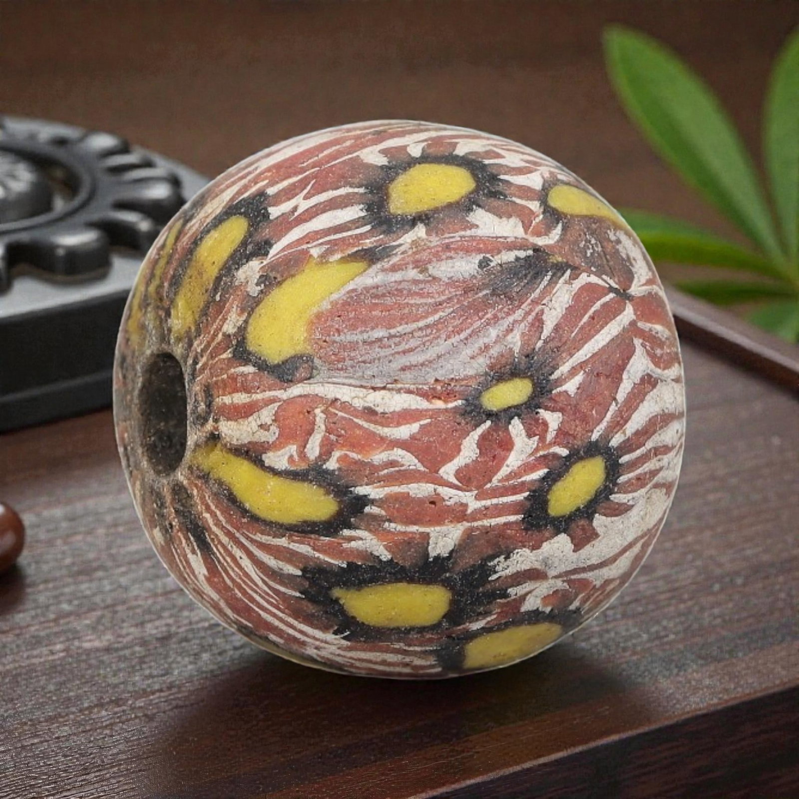 Antique Glass Bead - Islamic Jatim Red Floral Mosaic, 70YH: A spherical glass bead of Islamic Jatim type, crafted from polychrome mosaic glass. The surface features repeating stylized floral motifs with bright yellow centers and black outlines, set against a s