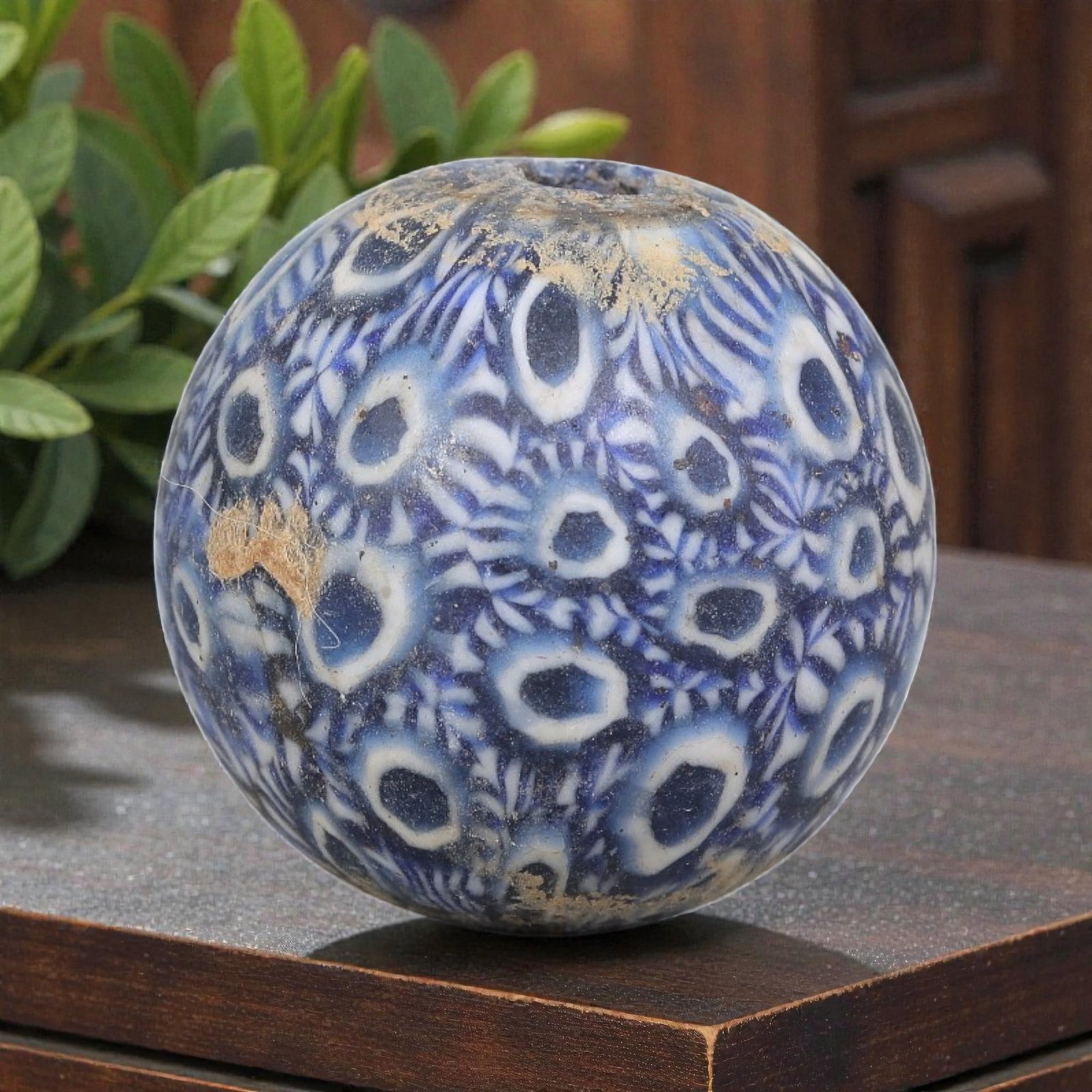 Antique Glass Bead - Islamic Jatim Blue-White Peacock Feather Mosaic, 51YH: A spherical glass bead of Islamic Jatim type, crafted from polychrome mosaic glass. The surface features a dense pattern of repeating eye motifs with dark blue centers framed by white rings, intersper