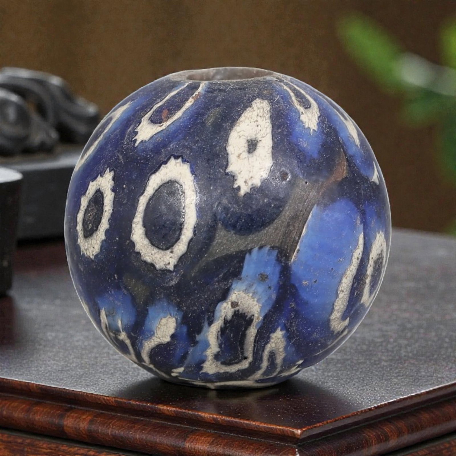 Antique Glass Bead - Islamic Jatim Indigo Eye Mosaic, 69YH: A spherical glass bead of Islamic Jatim type, crafted from polychrome mosaic glass. The surface features bold, irregular eye motifs with dark centers and white, cracked borders, set against a deep ind