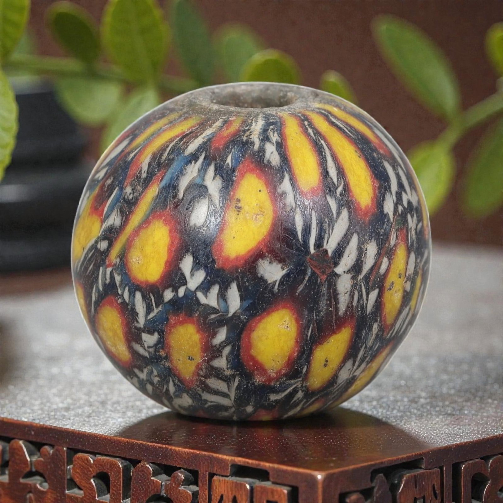 Antique Glass Bead - Islamic Jatim Yellow Peacock Eye Mosaic, 75AP: A spherical glass bead of Islamic Jatim type, crafted from polychrome mosaic glass. The surface features repeating peacock eye motifs with bright yellow centers and red borders, set against a deep blu