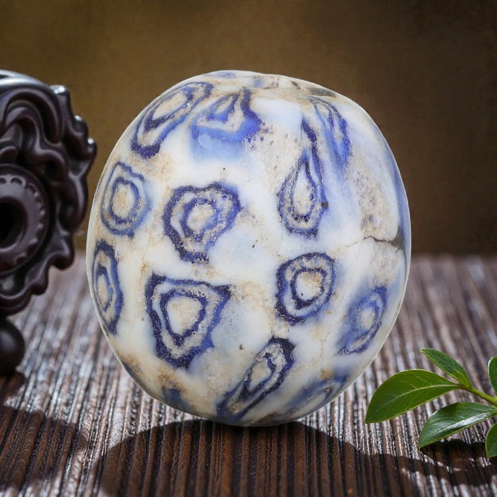 Antique Glass Bead - Islamic Jatim White-Blue Swirl Eye Mosaic, 46YH: A spherical glass bead of Islamic Jatim type, crafted from polychrome mosaic glass. The surface features irregular, swirling eye motifs outlined in deep blue, set against a soft white and pale blue ma