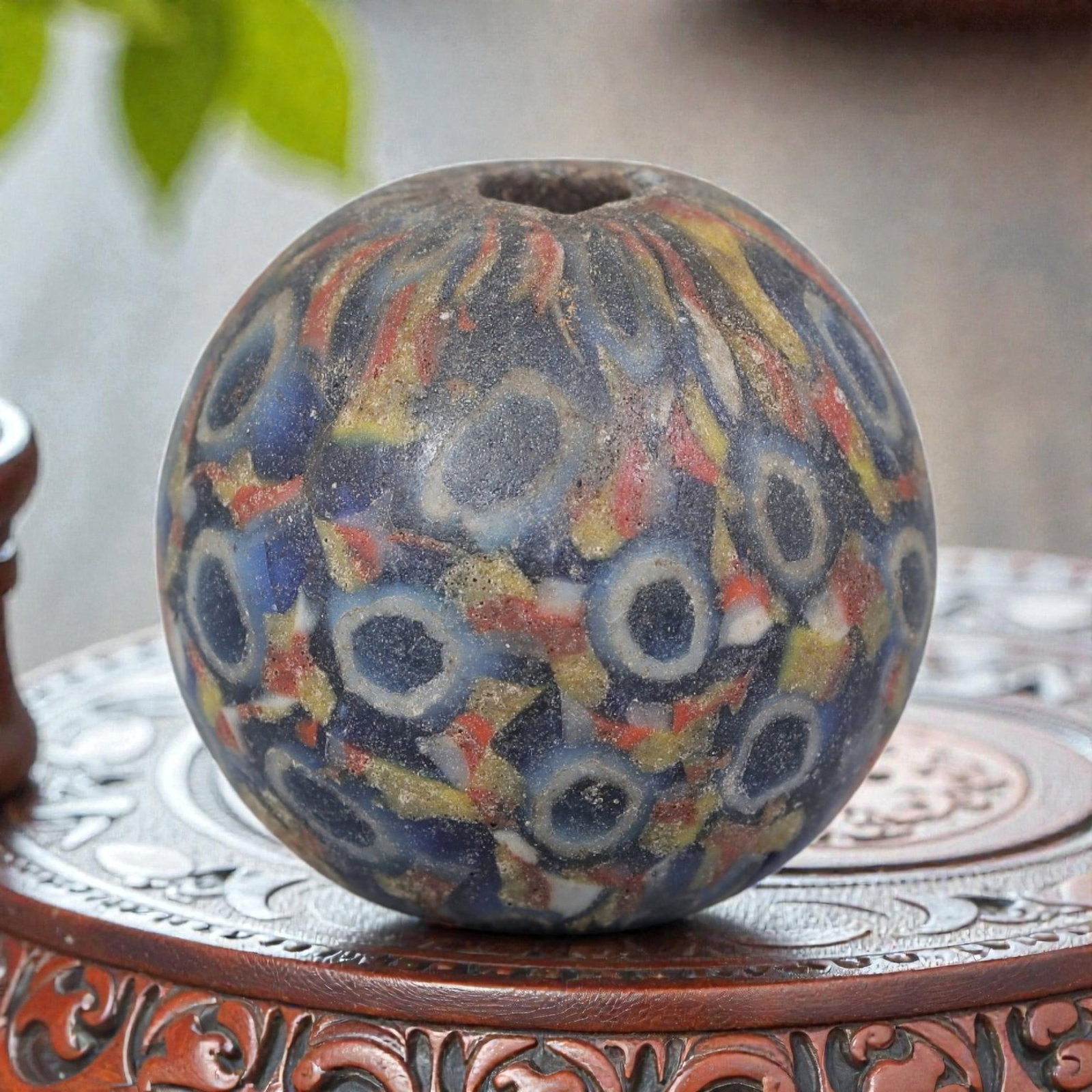 Antique Glass Bead - Islamic Jatim Multicolor Eye Mosaic, 72AP: A spherical glass bead of Islamic Jatim type, crafted from polychrome mosaic glass. The surface features repeating eye motifs set against a dark blue ground, interspersed with vibrant red, yellow, and