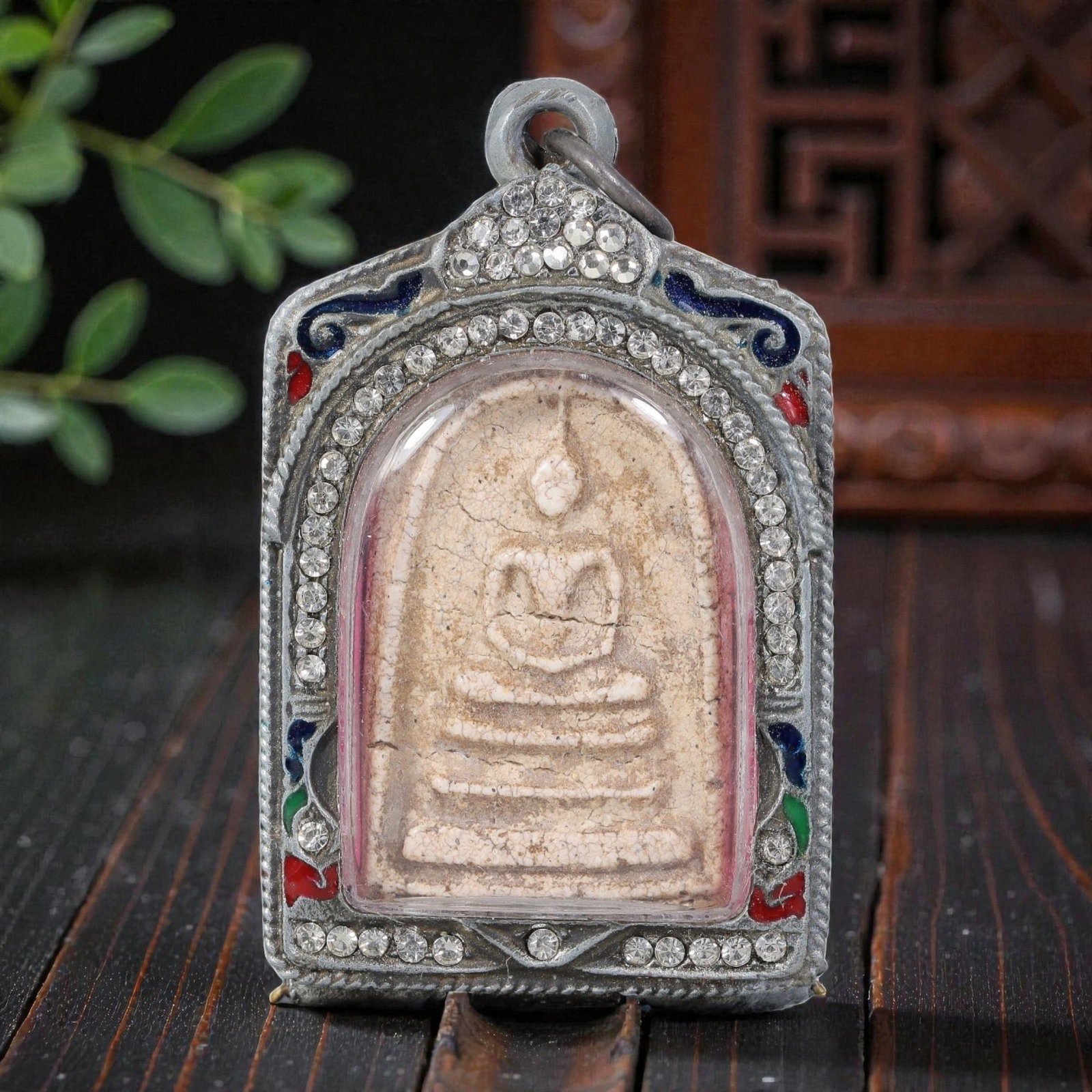 Thai Buddha Amulet - Crystal Enamel Silver Tone Pendant, 55AP: A Thai Buddhist amulet featuring a seated Buddha figure on tiered bases, housed in a silver-tone metal casing. The glass-fronted enclosure protects the aged, cracked Buddha plaque, which displays a pa