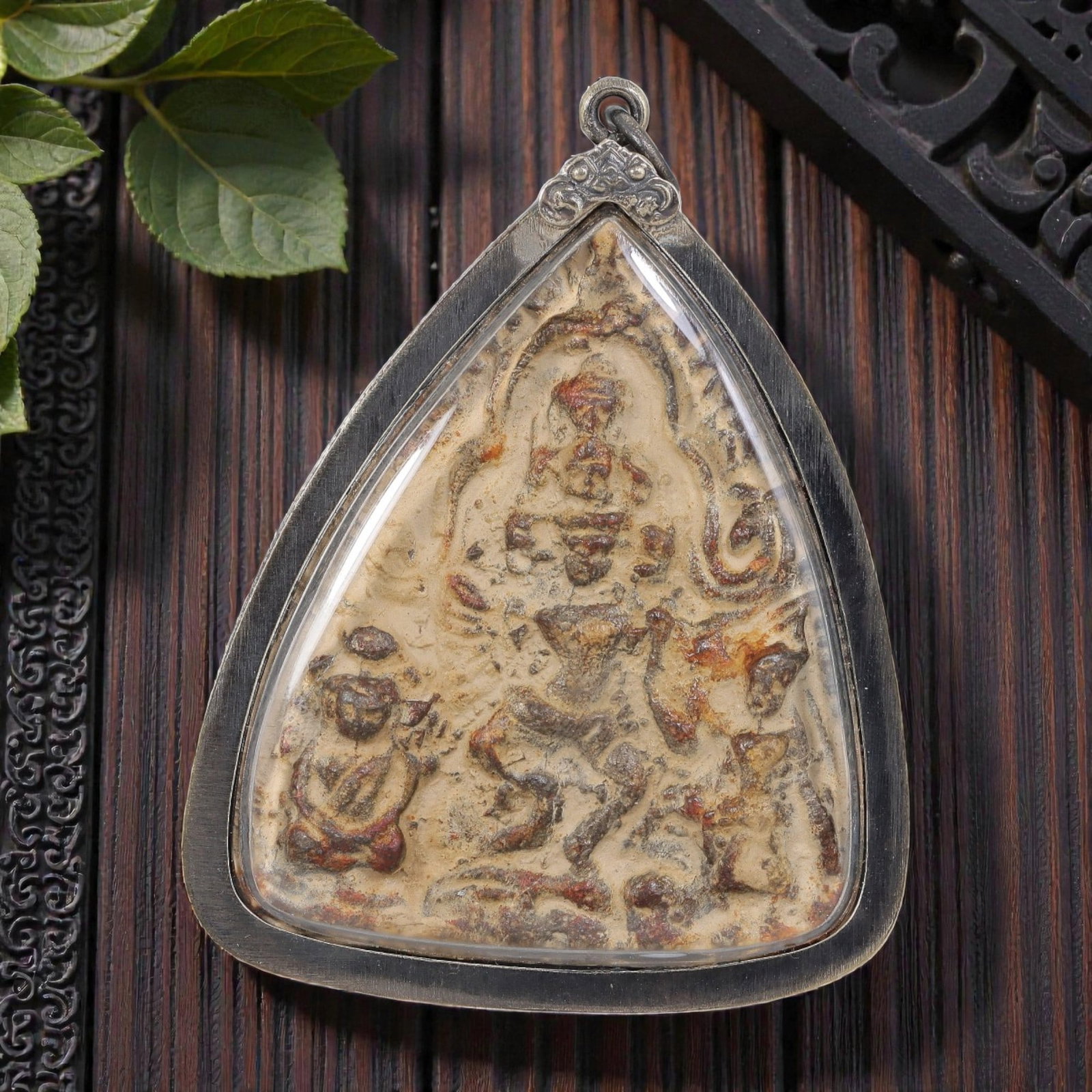 Thai Buddha Amulet - Triangular Silver Tone Pendant, 45AP: A Thai Buddhist amulet featuring a central deity figure with attendant figures, housed in a triangular silver-tone metal casing with a glass-fronted enclosure. The amulet plaque displays aged patina a