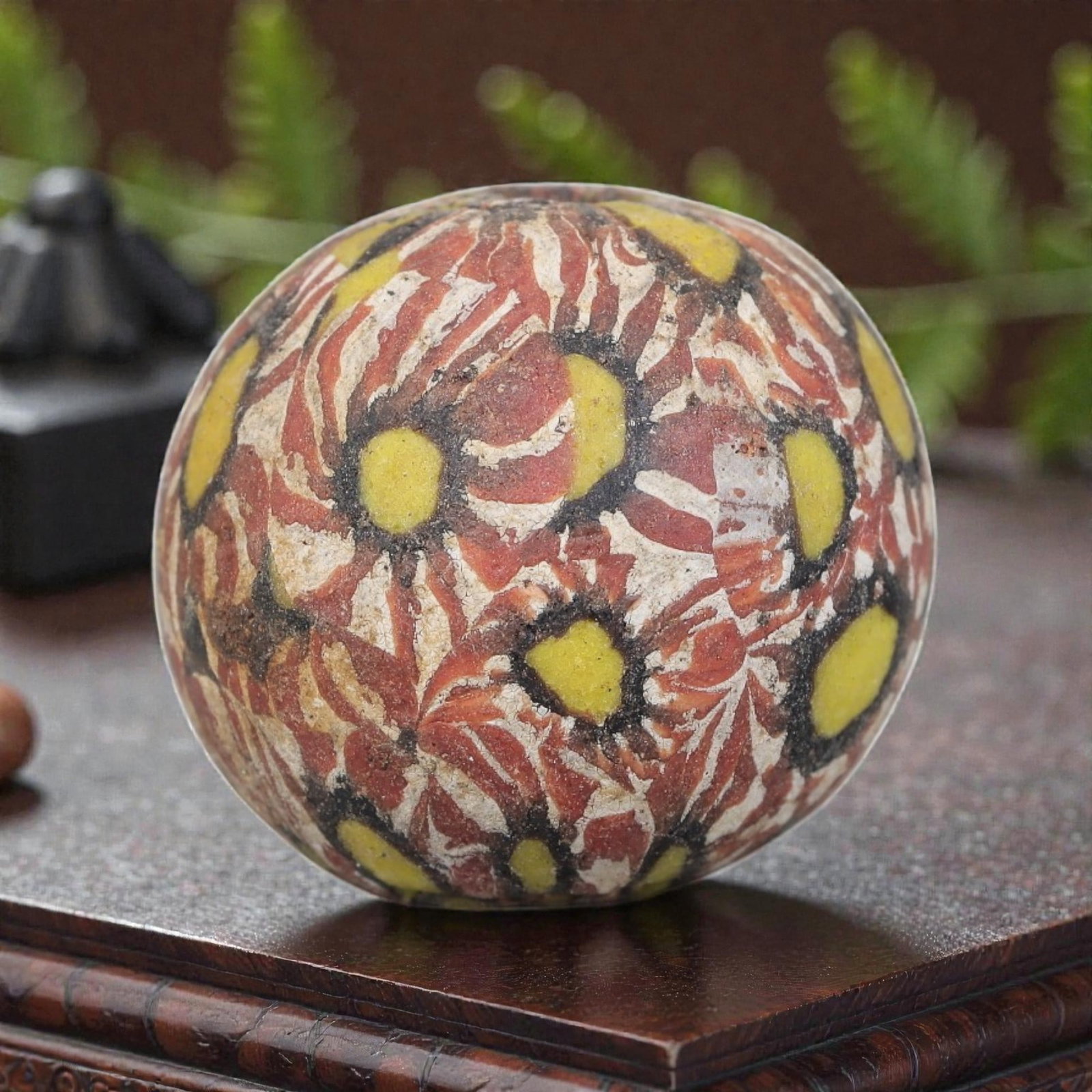 Antique Glass Bead - Islamic Jatim Red Floral Mosaic, 63AP: A spherical glass bead of Islamic Jatim type, crafted from polychrome mosaic glass. The surface features an intricate red floral mosaic pattern, with bold yellow accents set within a marbled red and w