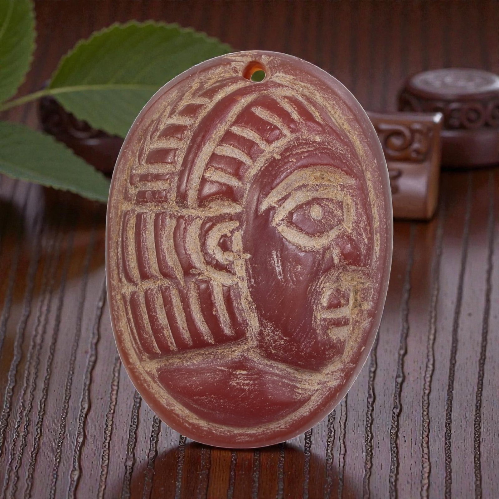 Antique Egyptian Carnelian Intaglio with Profile Head Motif, 100AN: Carved from carnelian with rich reddish-orange coloration, the oval-shaped intaglio features an incised profile head of a figure wearing a detailed headdress. The carving includes defined facial featu
