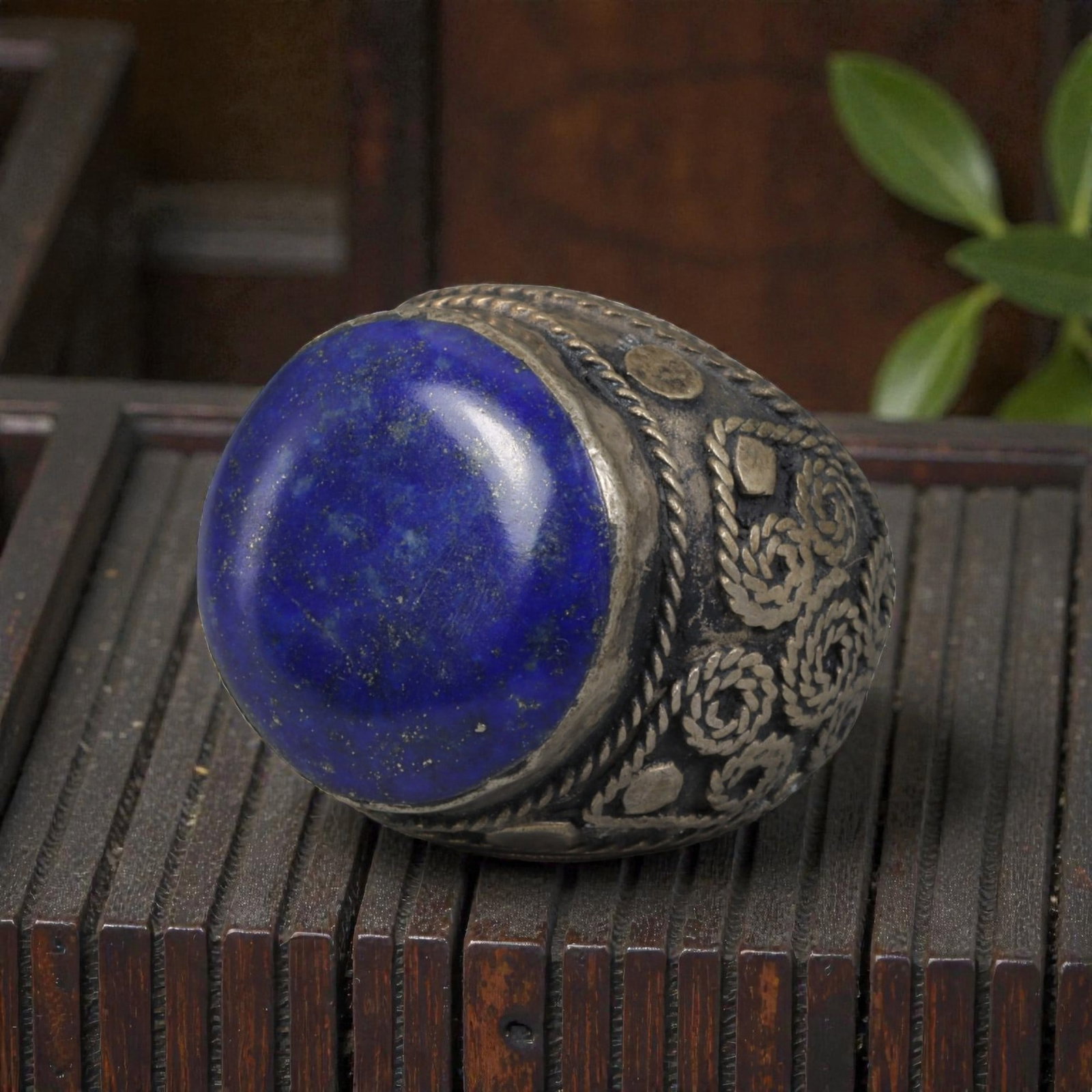 Antique Central Asian Silver and Lapis Lazuli Tribal Ring, 19th-Early 20th Century, 55AJ: The ring is set with a large, smooth cabochon lapis lazuli stone, exhibiting natural pyrite inclusions within its deep blue matrix. The silver mount is decorated with pseudo-filigree wirework and appl