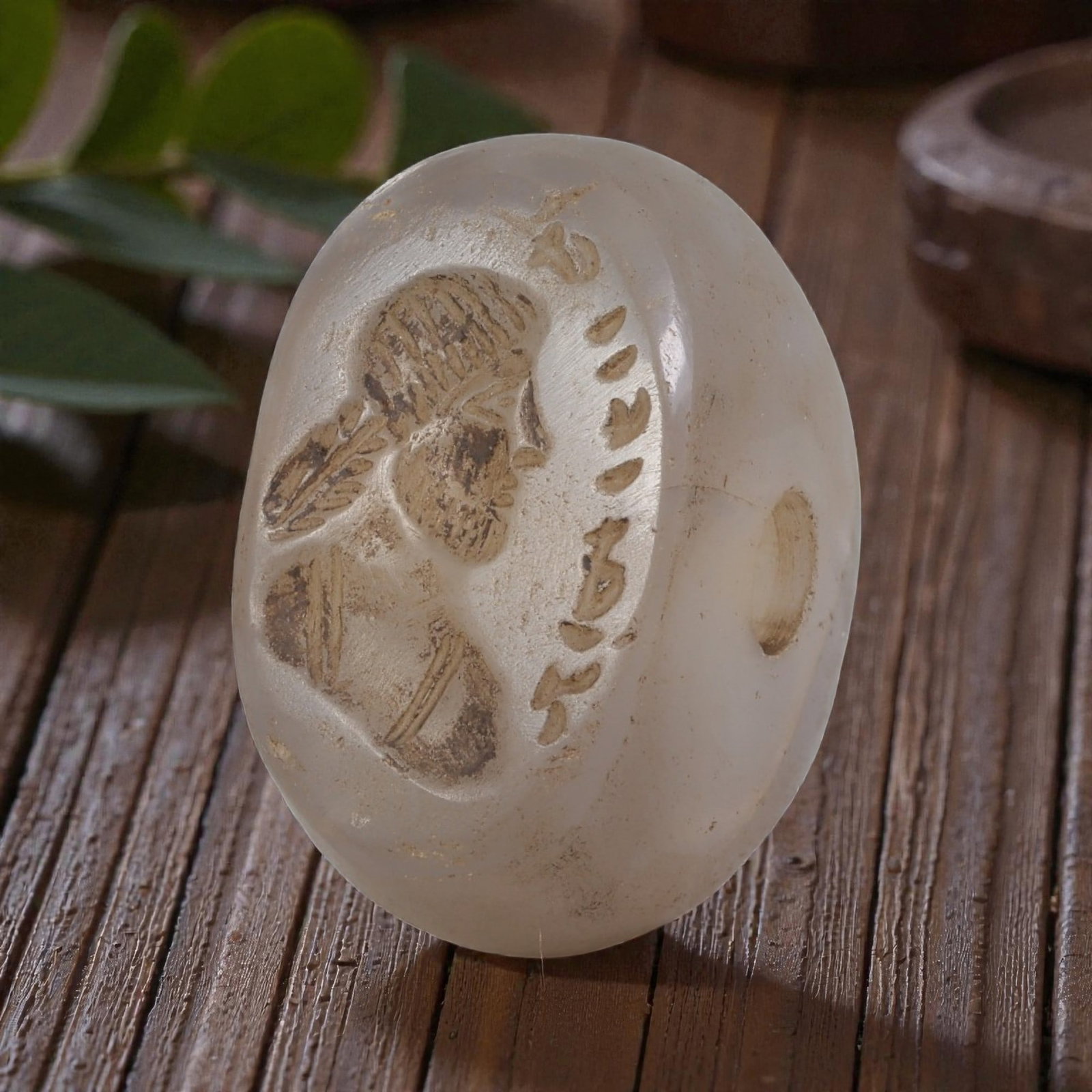 Ancient Sasanian Chalcedony Anthropomorphic Stamp Seal, 71YD: This ancient stamp seal is carved from translucent white chalcedony, with a domed, lenticular form and a central perforation for suspension. The flat face bears a finely engraved intaglio depicting a 