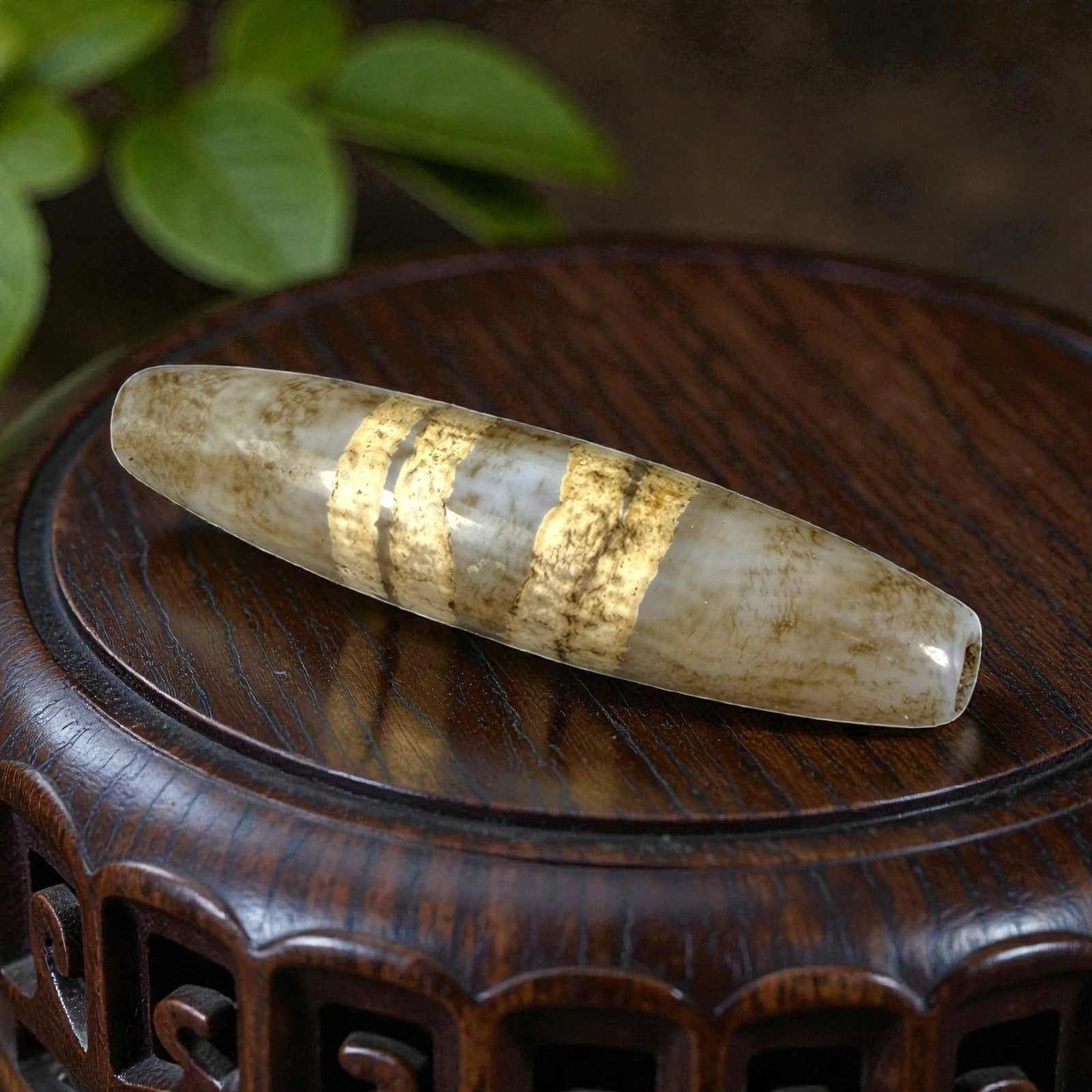Antique Himalayan Tibetan Agate Etched Chung Dzi Bead, 35AN: Elongated and cylindrical in form, the bead is carved from natural agate with a translucent, light-toned base exhibiting natural banding and brownish inclusions. Two wide, parallel gold-toned etched b