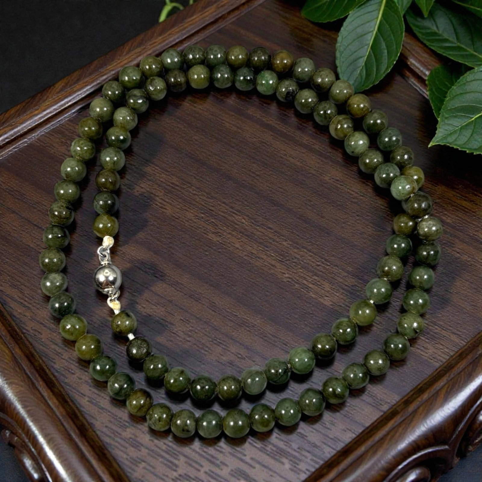 Chinese Jadeite Jade Bead Necklace, 20th Century, 96XE: A continuous strand of polished jadeite beads, each of uniform spherical form, displaying deep forest green and olive tones with natural mineral inclusions and subtle variations in translucency. The b