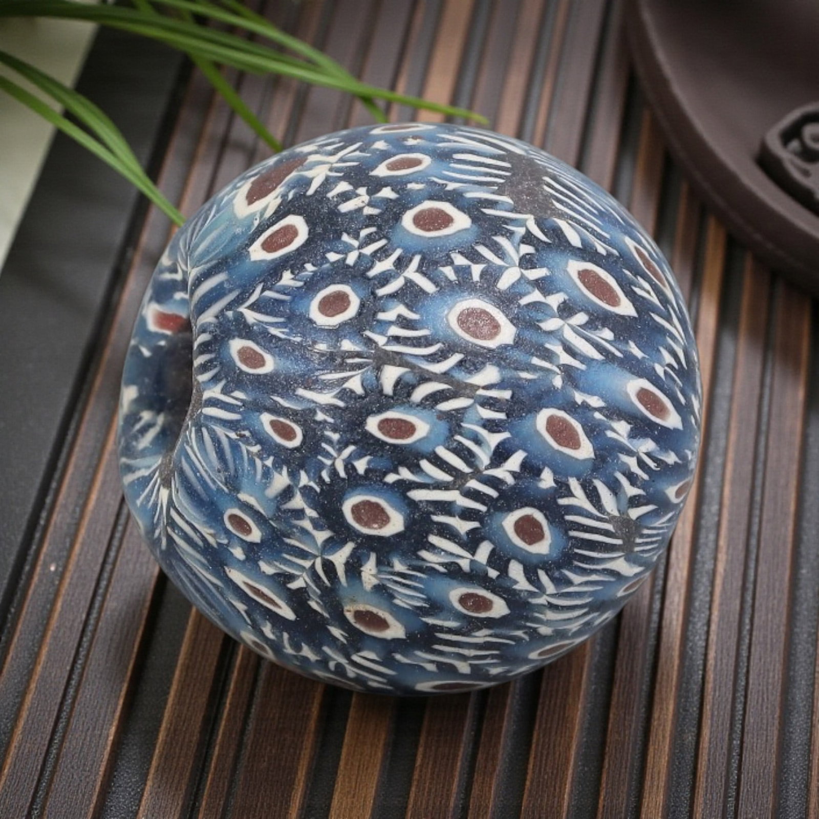 Antique Glass Bead - Islamic Jatim Indigo Peacock Feather Mosaic, 66YH: A spherical glass bead of Islamic Jatim type, crafted from polychrome mosaic glass. The surface features a dense peacock feather motif, with repeating eye patterns (brown centers, white rings) intersp