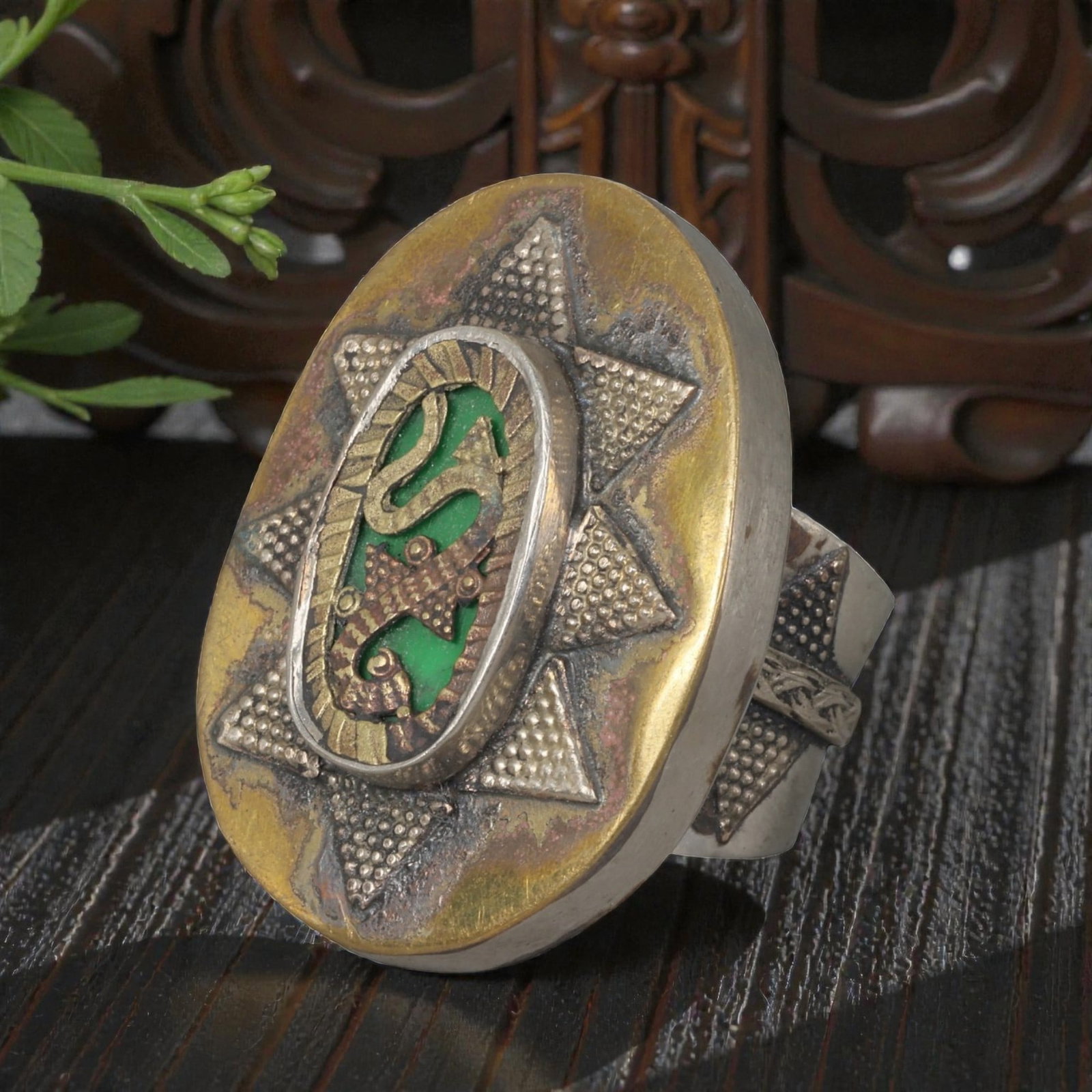 A Central Asian Silver Plated Gecko Motif Ring, Late 19th-Early 20th Century, 26AK: Crafted from silver plated metal with brass accents, featuring a wide, open band. The oval bezel displays a central inlaid panel with a green background, overlaid with a gecko motif in contrasting met