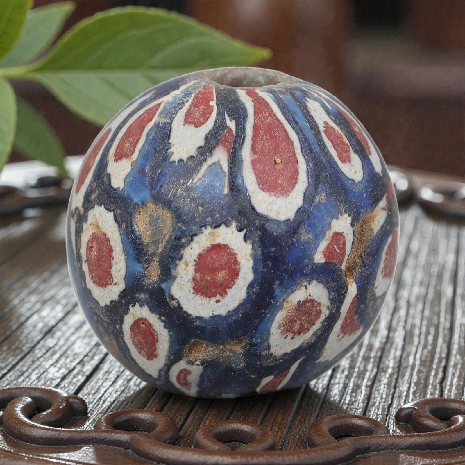 Antique Glass Bead - Islamic Jatim Red Eye Mosaic, 69AP: A spherical glass bead of Islamic Jatim type, crafted from polychrome mosaic glass. The surface features repeating red eye motifs with white borders, set against a deep blue ground. The design include