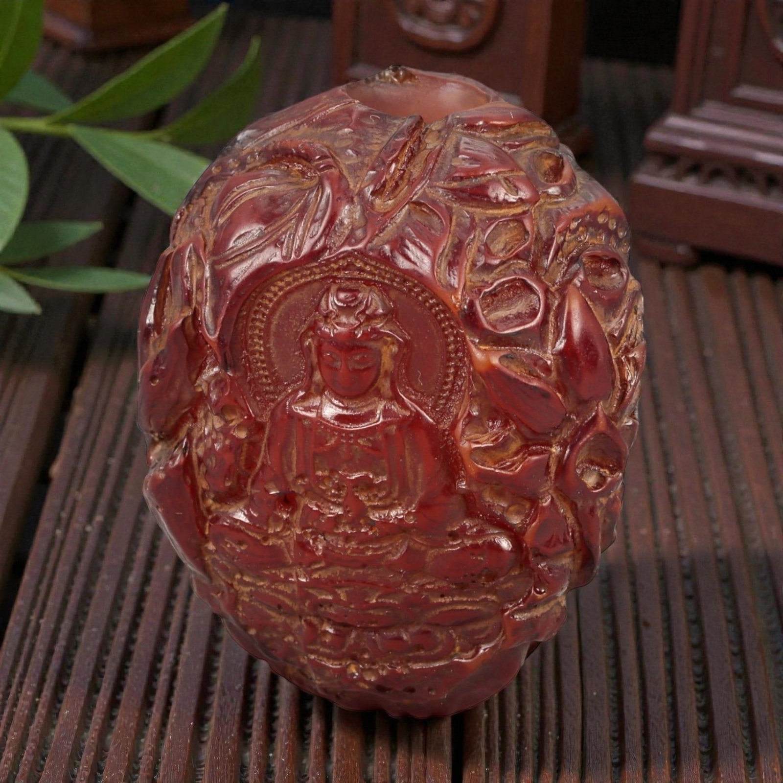 A Buddhist Amber-Resin Bead, 20th Century, 79FC: Molded from translucent reddish-brown amber-colored resin with lighter inclusions and surface variation, the object is formed as a bead carved in relief with Buddhist imagery. One face depicts a seate
