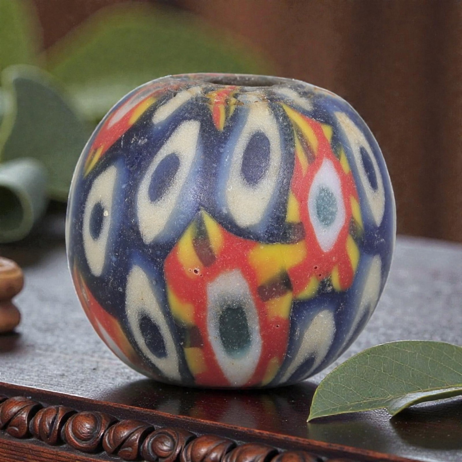 Antique Glass Bead - Islamic Jatim Multicolor Eye Mosaic, 42YH: A spherical glass bead of Islamic Jatim type, crafted from polychrome mosaic glass. The surface features repeating eye motifs in two distinct color schemes: one with dark blue centers framed by creamy