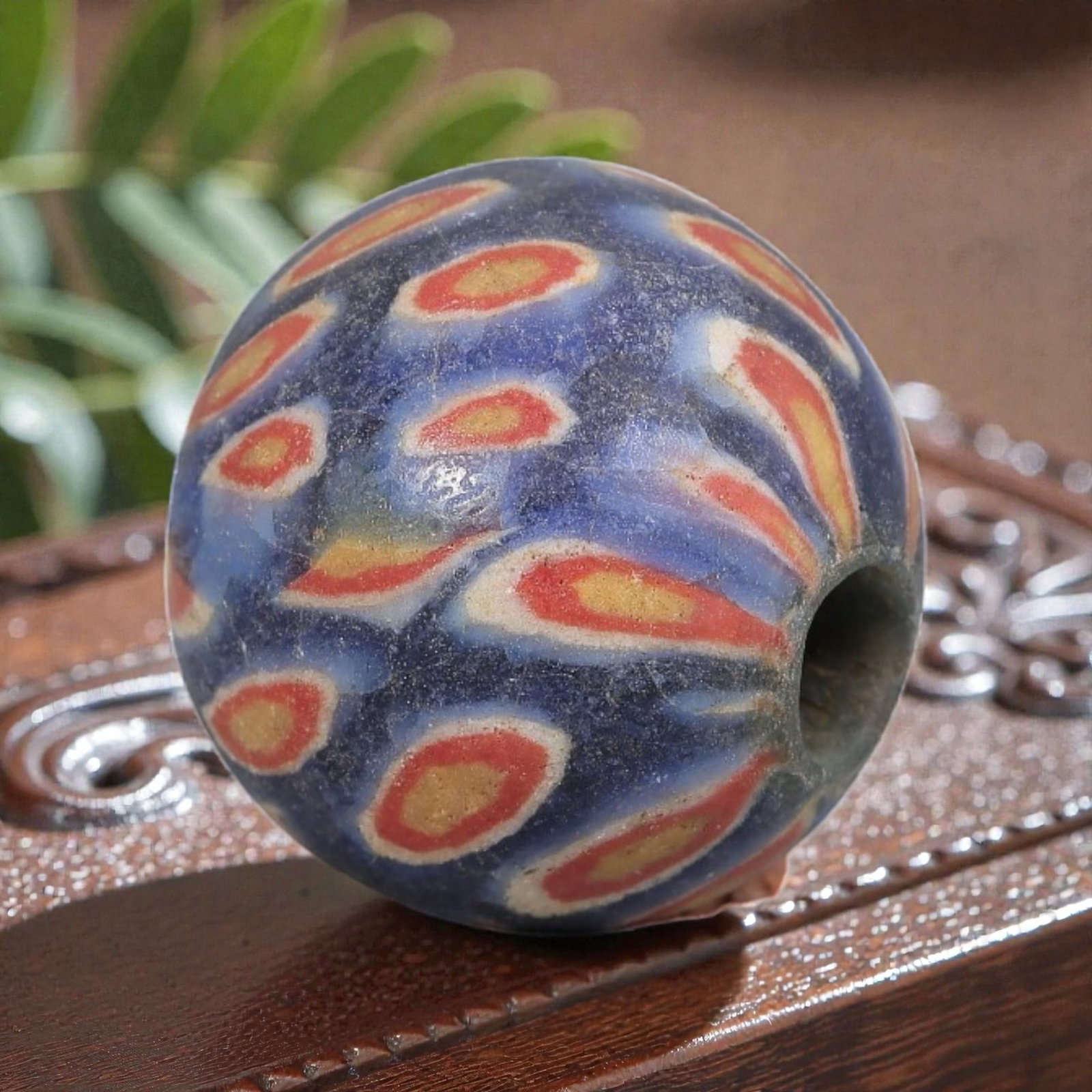 Antique Glass Bead - Islamic Jatim Blue-Red-Yellow Eye Mosaic, 67YH: A spherical glass bead of Islamic Jatim type, crafted from polychrome mosaic glass. The surface features repeating eye motifs with yellow centers framed by red and white rings, set against a textured 