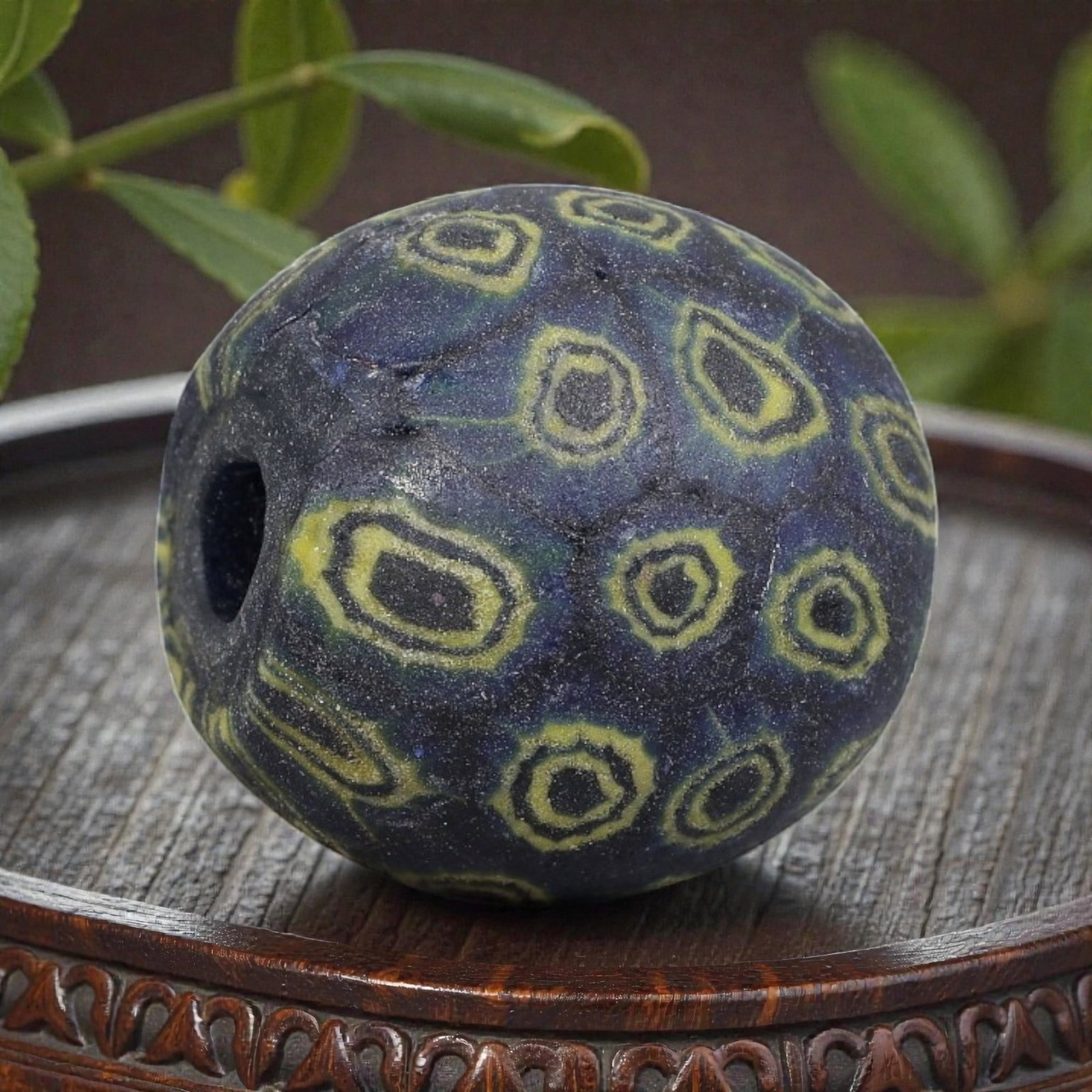 Antique Glass Bead - Islamic Jatim Indigo Yellow Concentric Eye Mosaic, 64YH: A spherical glass bead of Islamic Jatim type, crafted from polychrome mosaic glass. The surface features repeating concentric eye motifs with dark centers framed by bright yellow rings, set against a 