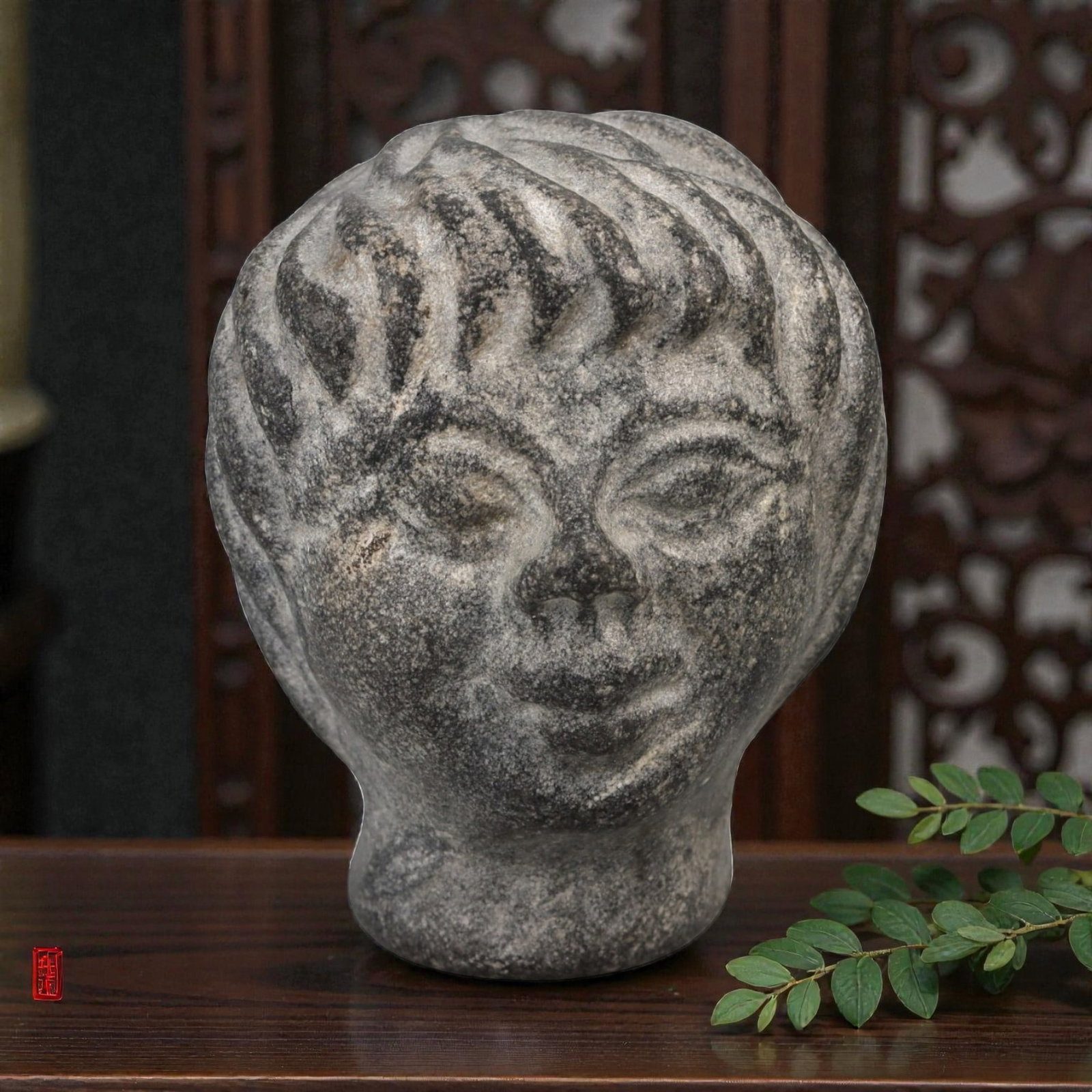 A Roman Stone Head, Circa 2nd-3rd Century CE, 3FT: Carved from a granular, dark grey stone with natural light inclusions, the object is a complete head, not a fragment, depicting a youthful male figure. The face is rendered with stylized features: alm