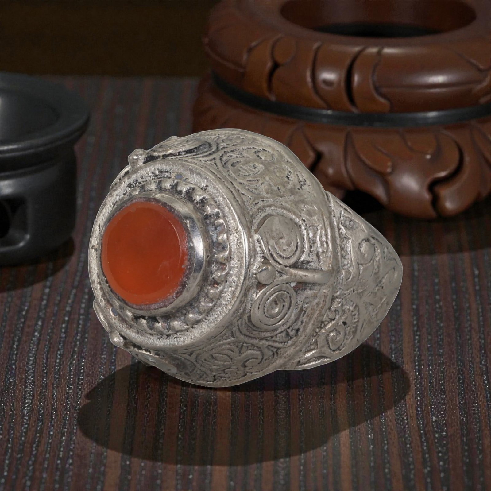 A Middle Eastern Silver Plated Carnelian Ring, Late 19th-Early 20th Century, 39AK: The ring is set with a round cabochon carnelian stone at the center of a domed bezel, framed by a raised, beaded border. The bezel and shoulders are decorated with incised scroll and spiral motifs, ch