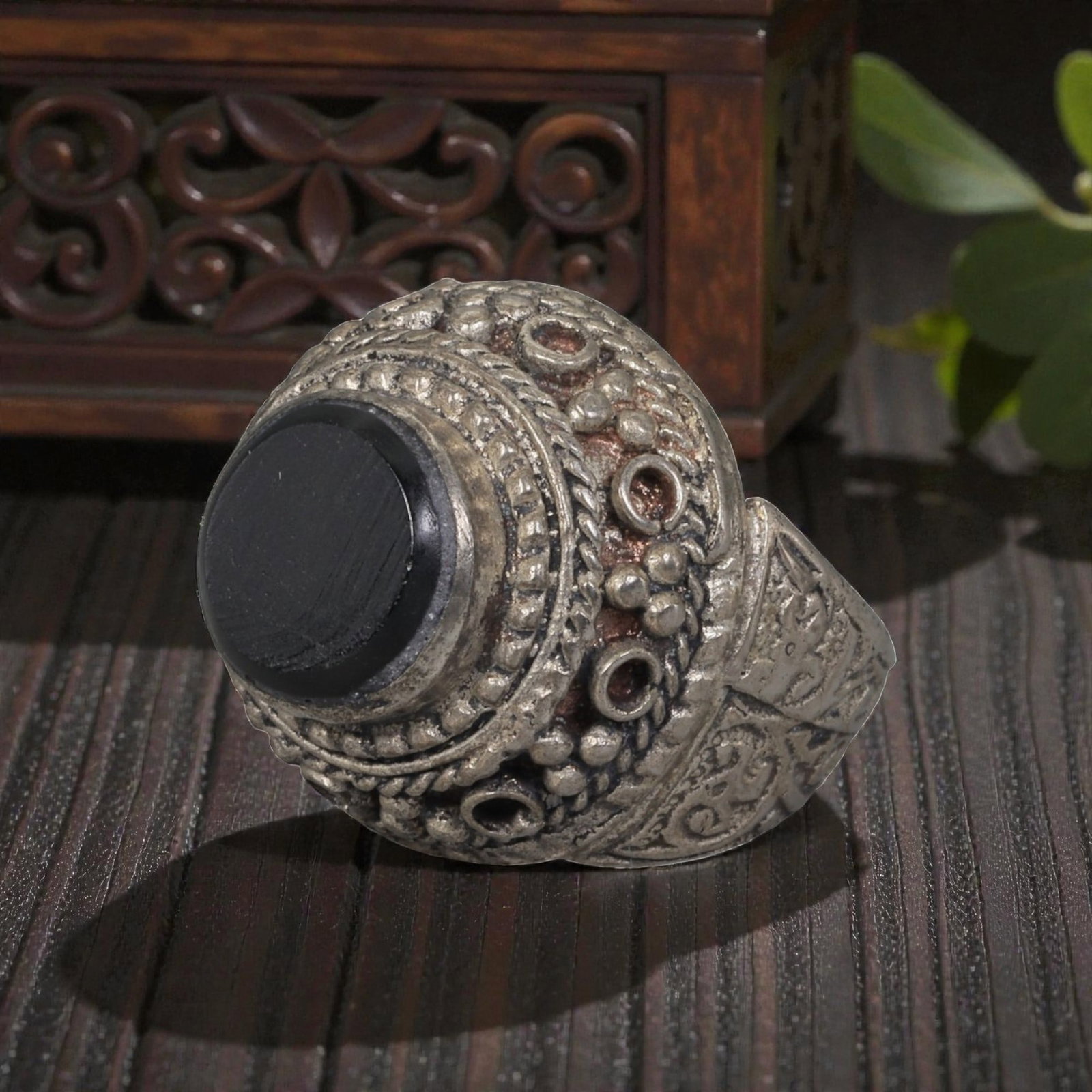 A Middle Eastern Silver Plated Onyx Ring, Late 19th-Early 20th Century, 32AK: The ring is centered with a round cabochon onyx stone set within a domed bezel decorated with beaded granulation, twisted wirework, and empty circular settings. The shoulders are engraved with scrolli