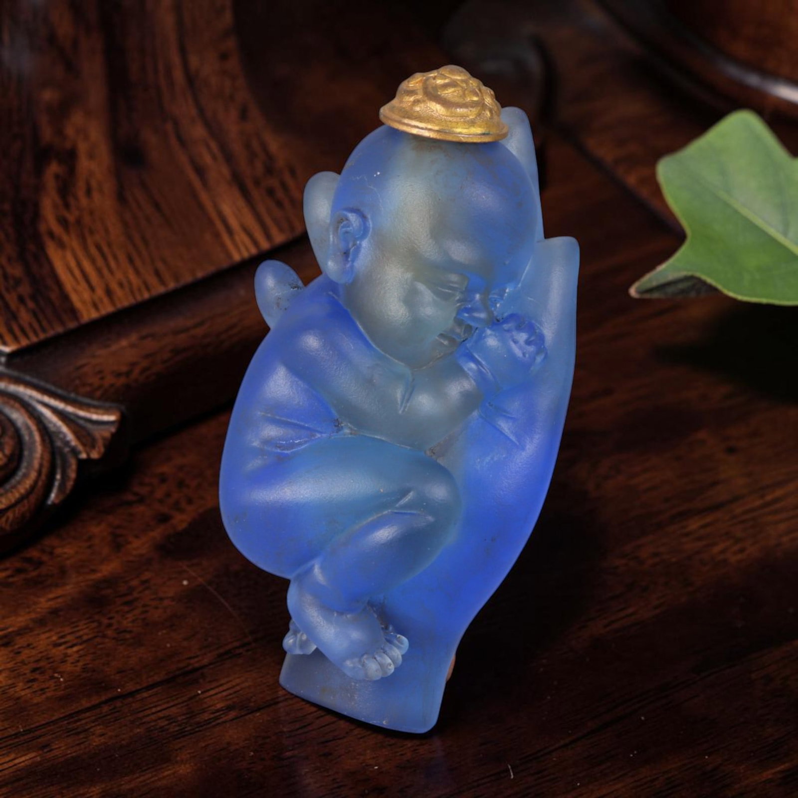 Vintage Chinese Liuli Glass Snuff Bottle - Sleeping Baby In Buddha Palm Sculpted Vessel, 36AS: This uniquely sculpted anthropomorphic snuff bottle is handcrafted from frosted translucent sky-blue vintage Chinese liuli glass, depicting a peacefully sleeping infant curled nestled within a detaile
