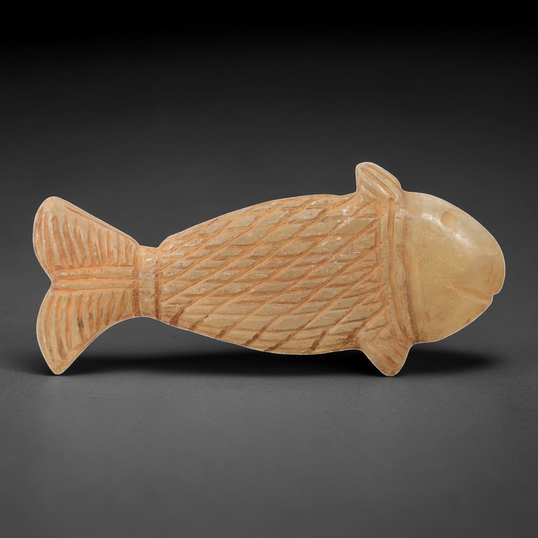 Ancient Chalcedony Fish - Near Eastern Amulet Figurine, 4AL: Carved from translucent chalcedony, this amulet depicts a stylized fish form with incised linear details defining the scales, fins, tail, and facial features, including a defined eye and mouth. Attrib