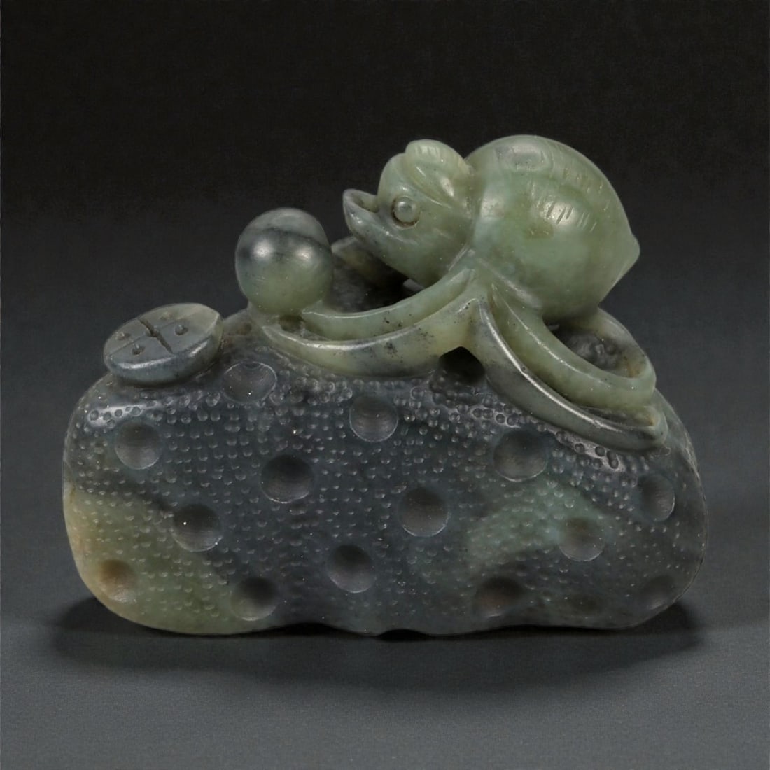 A Chinese Nephrite Jade Spider Carving, 20th Century, 78FB: Carved from dark green nephrite jade with mottled inclusions and areas of lighter translucency, the object is modeled as a spider resting upon a textured ground. The body is carved in the round, with 