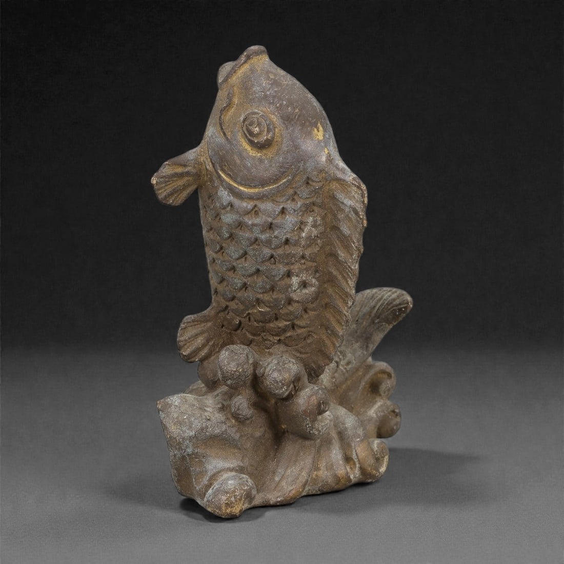 Old Chinese Bronze Fish Sculpture, Late Qing Dynasty, 19FH: Cast in bronze, the sculpture is formed as a single fish shown upright, emerging from stylized waves that serve as an integral base. The fish is rendered with a rounded head, prominent circular eye, a