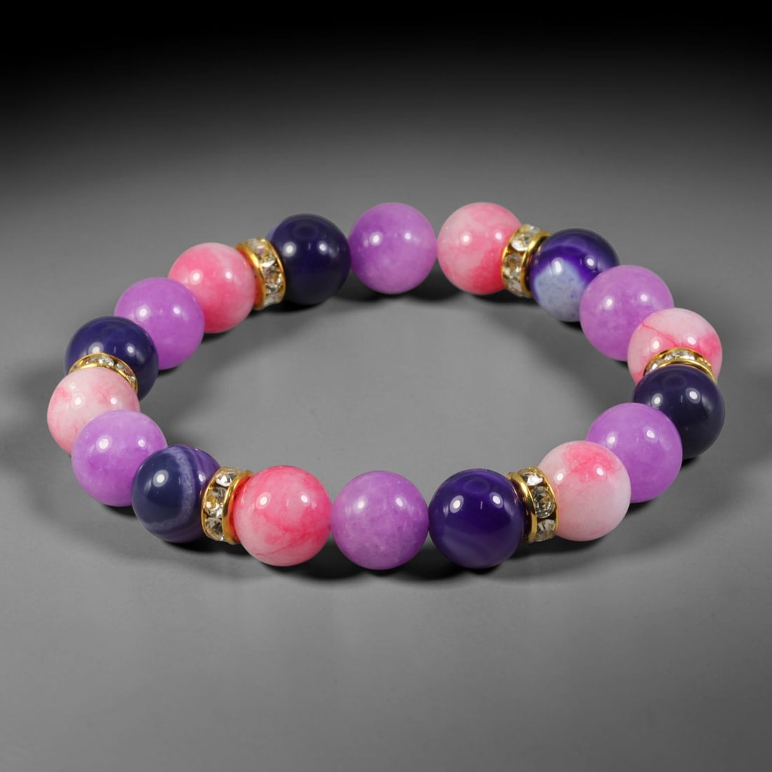Natural Mixed Stone Beaded Bracelet - Polished Round Bead Strand, 60FA: This elastic stretch bracelet is constructed from uniformly spherical polished natural mineral beads, interspersed with gold-toned metal spacers set with clear crystalline inlays. The hard stone exhib