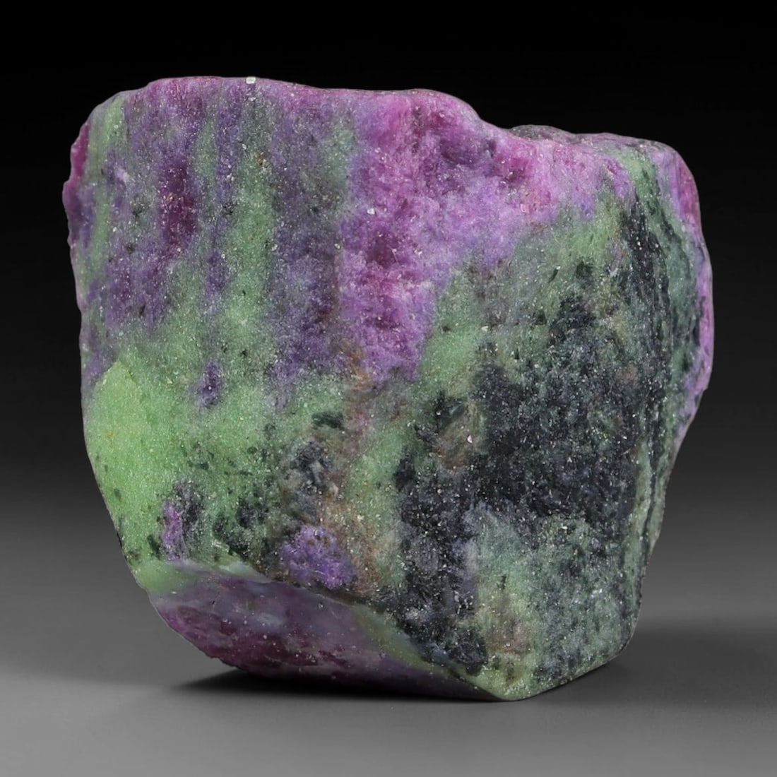 99ct Natural Tanzanian Ruby Zoisite Raw Rough Specimen Mineral Stone, 21FC: This unpolished mineral rough is natural ruby zoisite sourced from Tanzania, exhibiting distinct banded mineral segregation of vibrant green zoisite, magenta ruby crystals, and dark hornblende inclusi