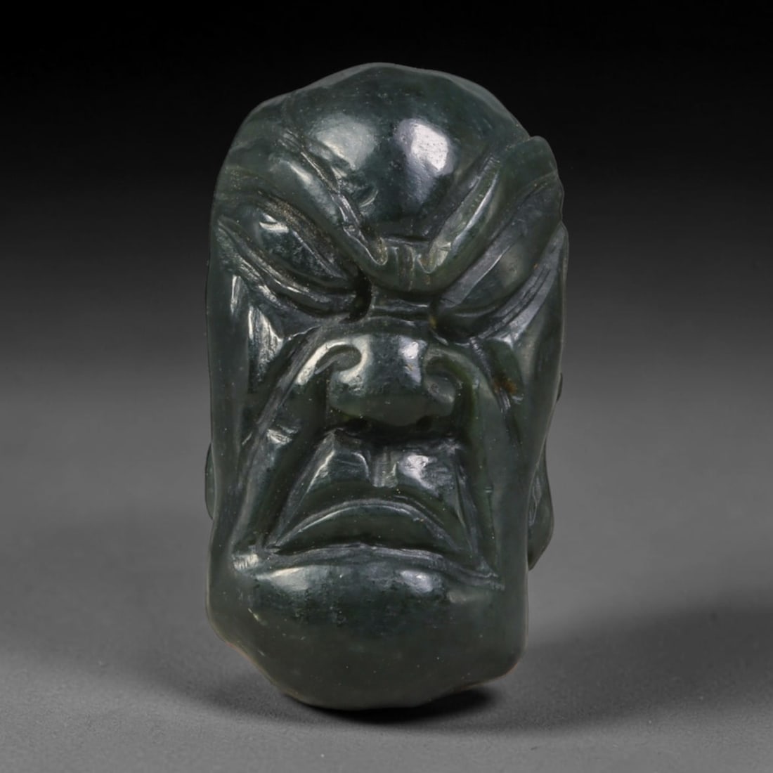 Natural Vintage Chinese Nephrite Jade Deep Dark Green Stern Arhat Head Carved Face Bead, 22AP: Hand-carved vintage Chinese strung bead crafted from natural vintage Chinese nephrite jade, measuring 3cm x 1.8cm. This barrel-form bead is sculpted into a stern, formidable Buddhist Arhat facial bust